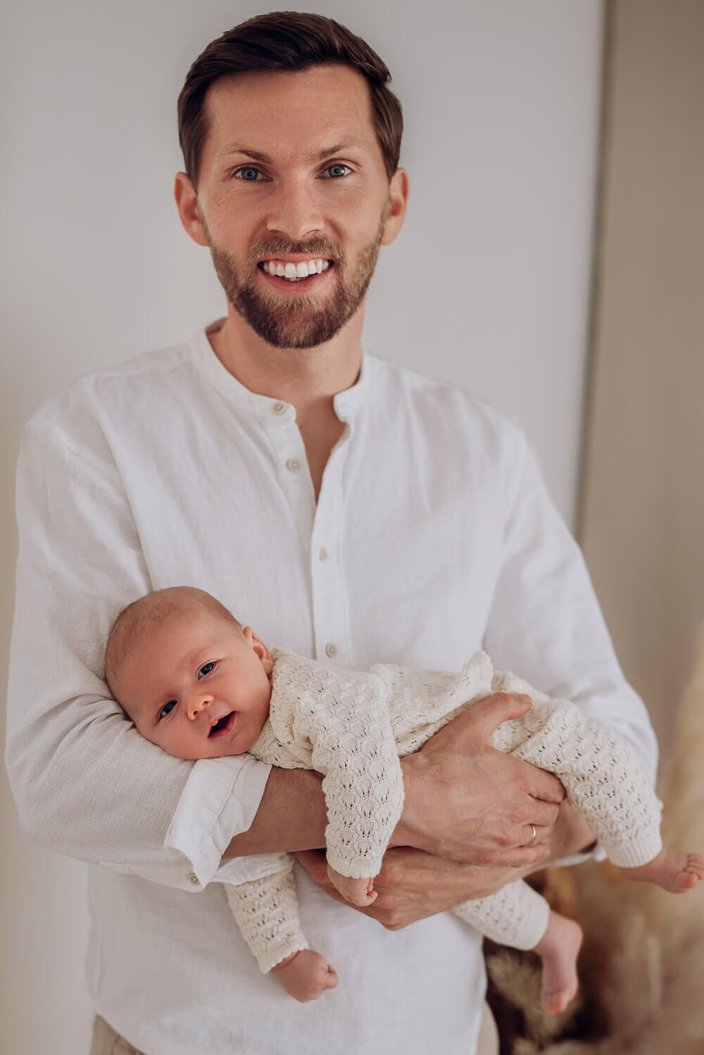 Authentisches Portrait im Fotostudio Hannover, Vater hält sein Baby im Arm und lächelt in die Kamera