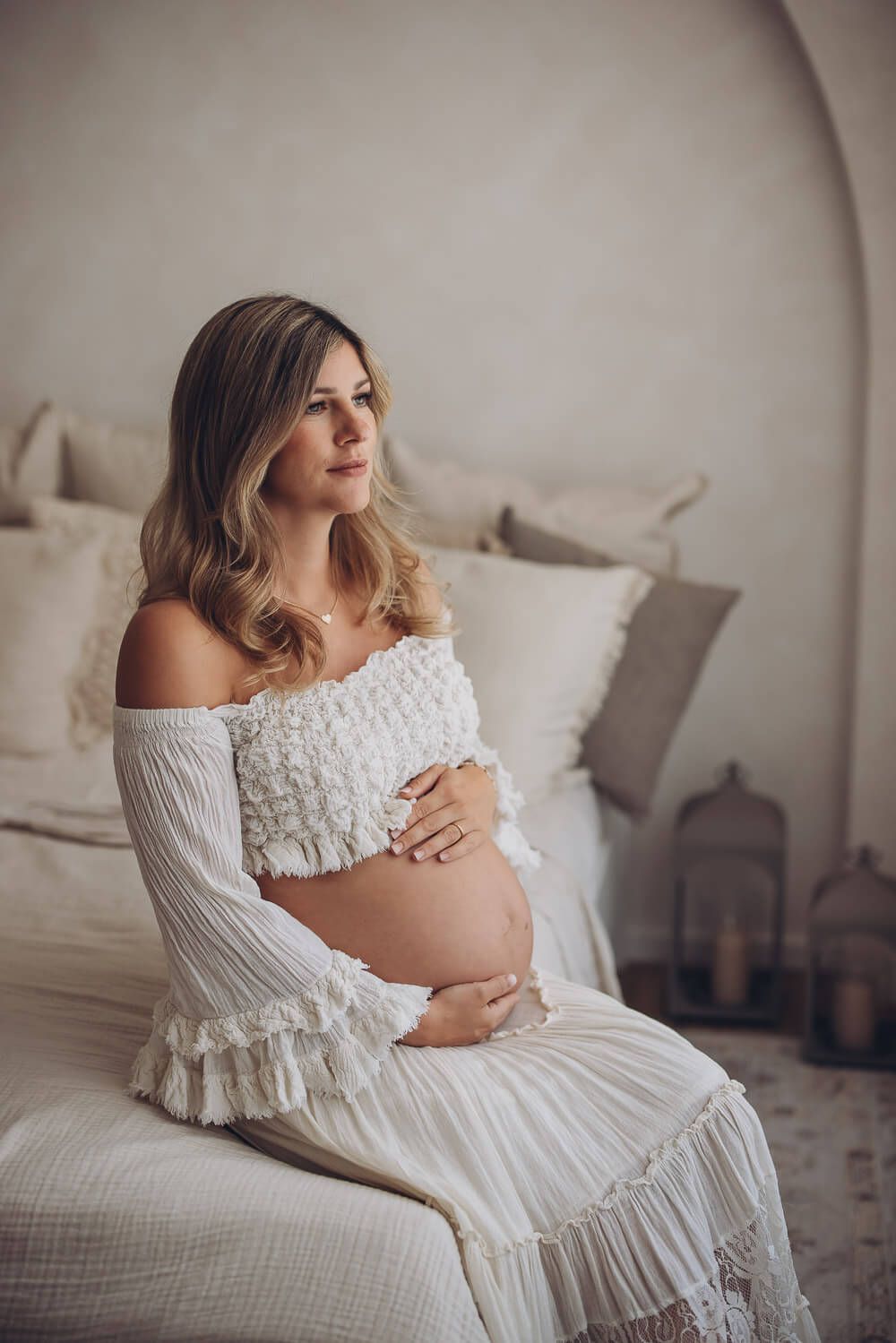 Ruhiges Babybauch Fotoshooting in Hameln – werdende Mutter sitzt auf dem Bett und umfasst ihren Bauch mit beiden Händen