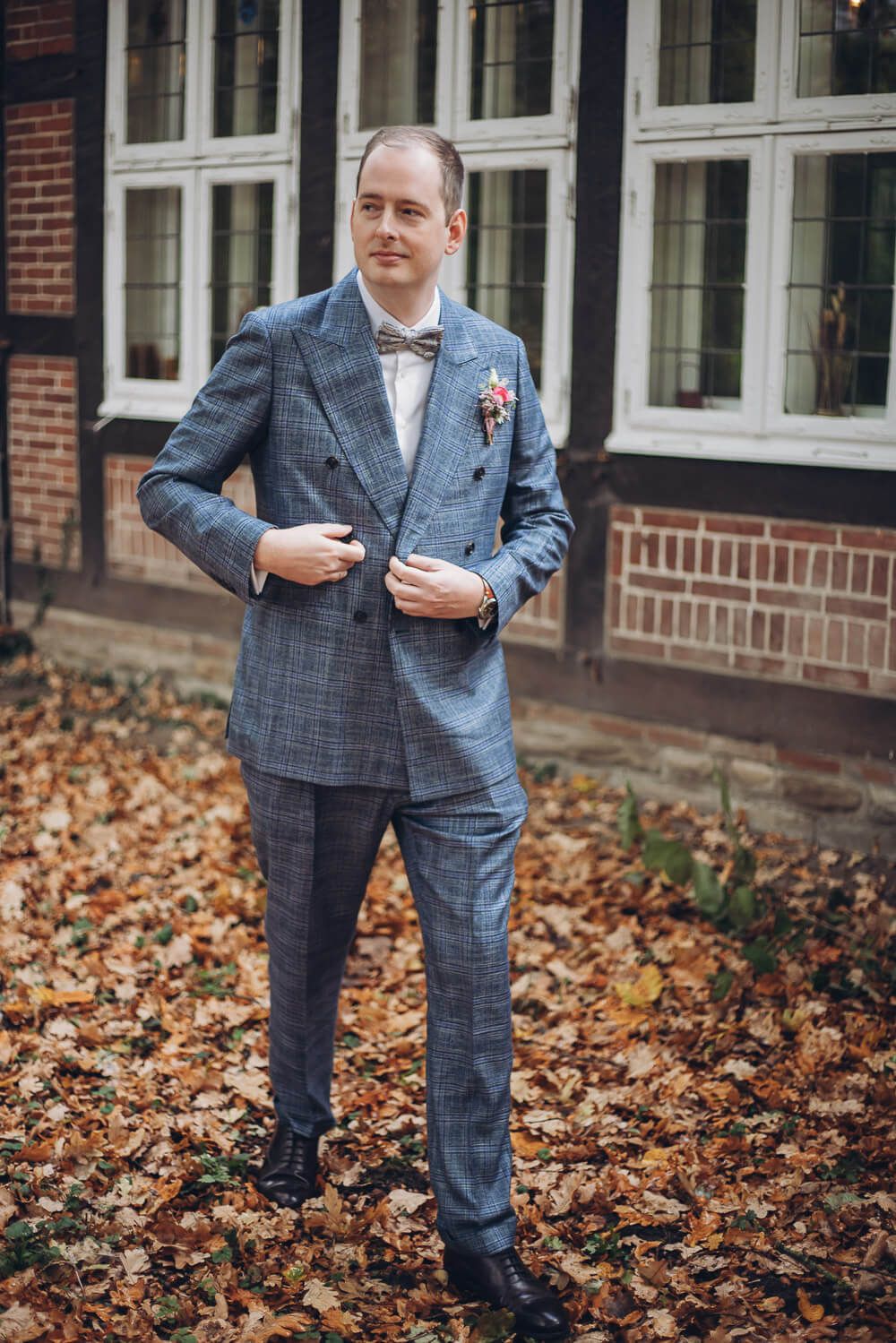 Bräutigam im blauen Anzug steht vor Fachwerkhaus im Herbst bei einer Hochzeit in Celle