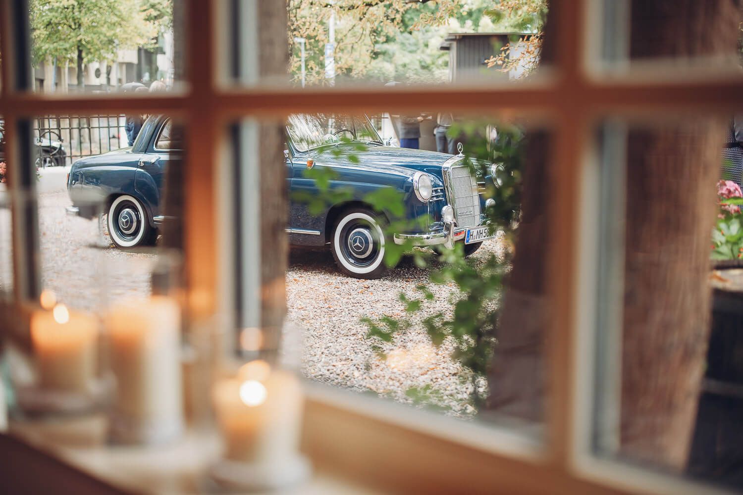 Blick durch ein Fenster auf einen blauen Hochzeitsoldtimer vor der Location, eingefangen von einem Hochzeitsfotografen aus Hannover