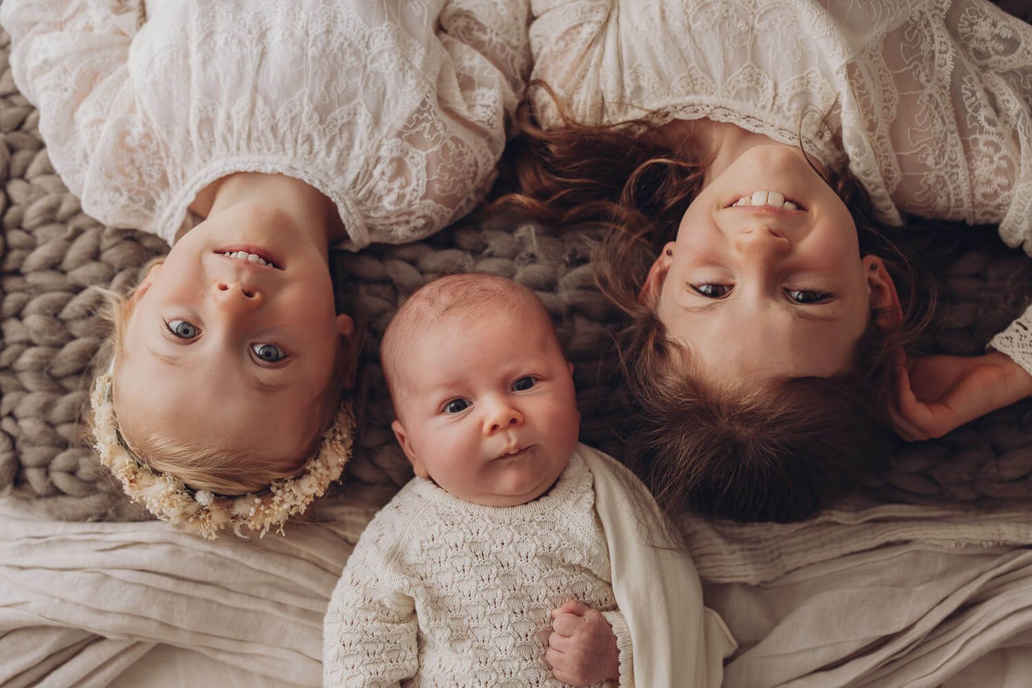 Liebevolle Geschwister liegen gemeinsam mit einem Baby im Fotostudio Hannover und schauen entspannt in die Kamera