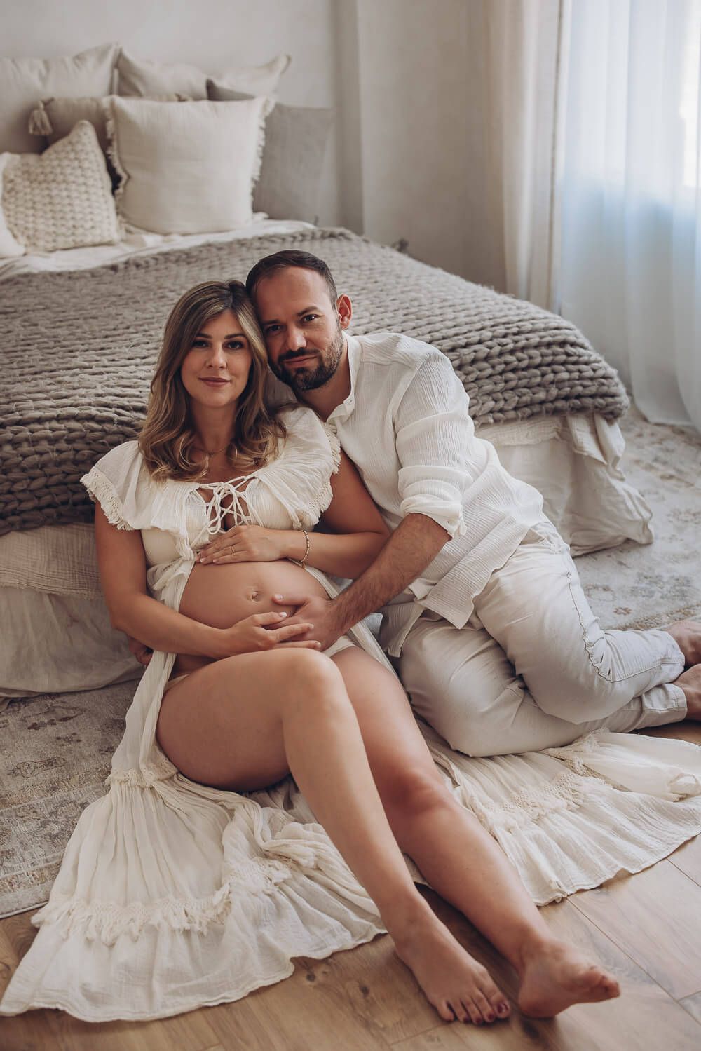Natürliches Babybauch Fotoshooting in Celle – werdende Eltern sitzen entspannt vor dem Bett und halten gemeinsam den Bauch