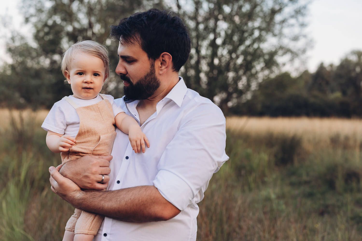 Authentisches Portrait beim Outdoor Shooting Hannover, Vater hält sein Baby liebevoll im Arm vor weicher Naturkulisse