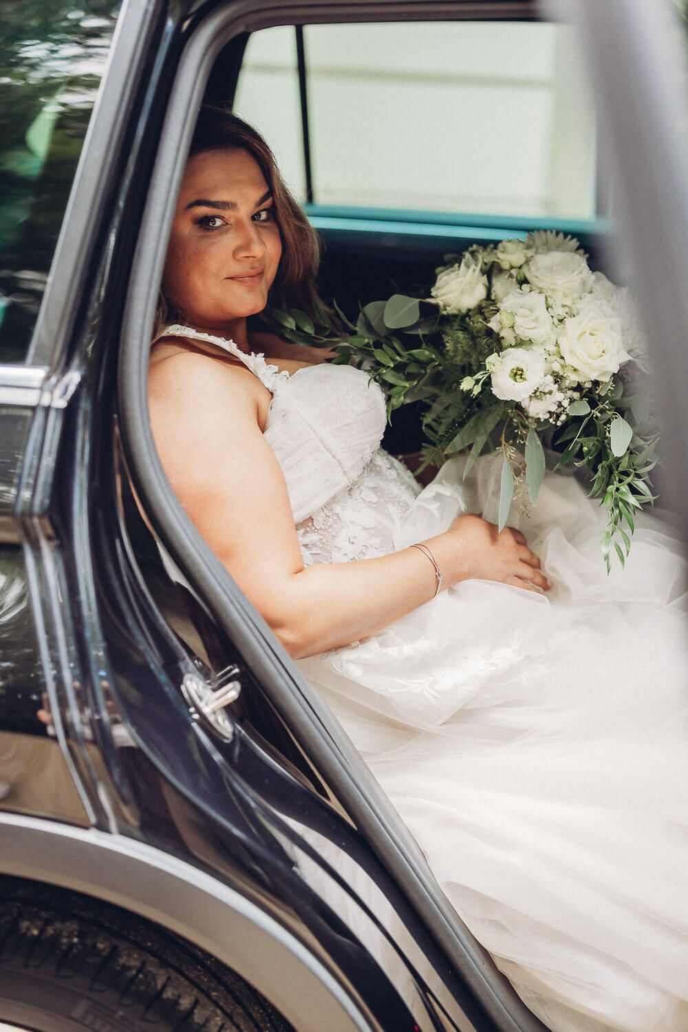 Braut sitzt mit großem weißen Brautstrauß im Hochzeitsauto, fotografiert von einer Hochzeitsfotografin in Hannover