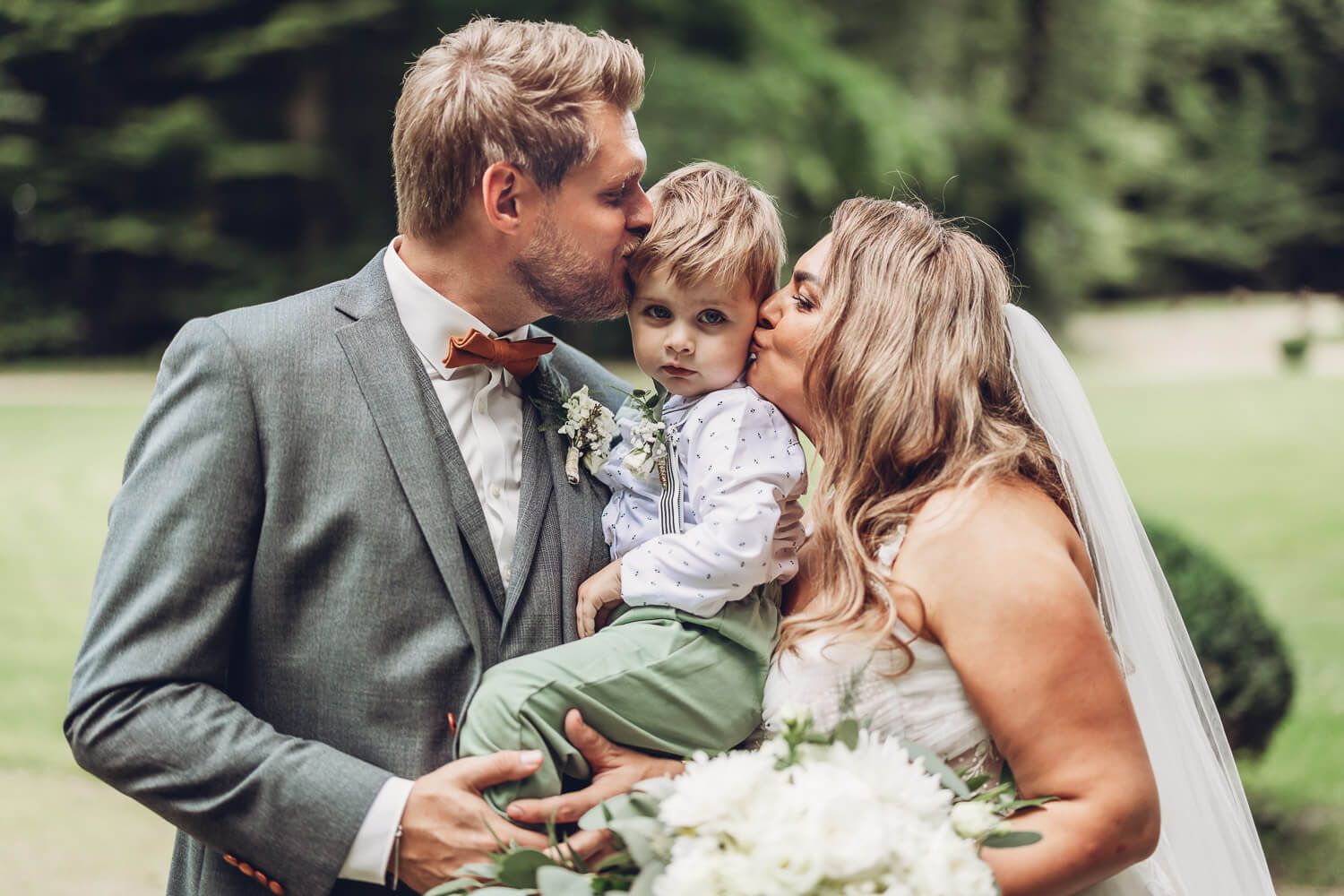 Liebevolles Familienfoto von Brautpaar und Kind im Grünen bei einer Hochzeit in Hannover - Hochzeitsfotograf Bad Nenndorf