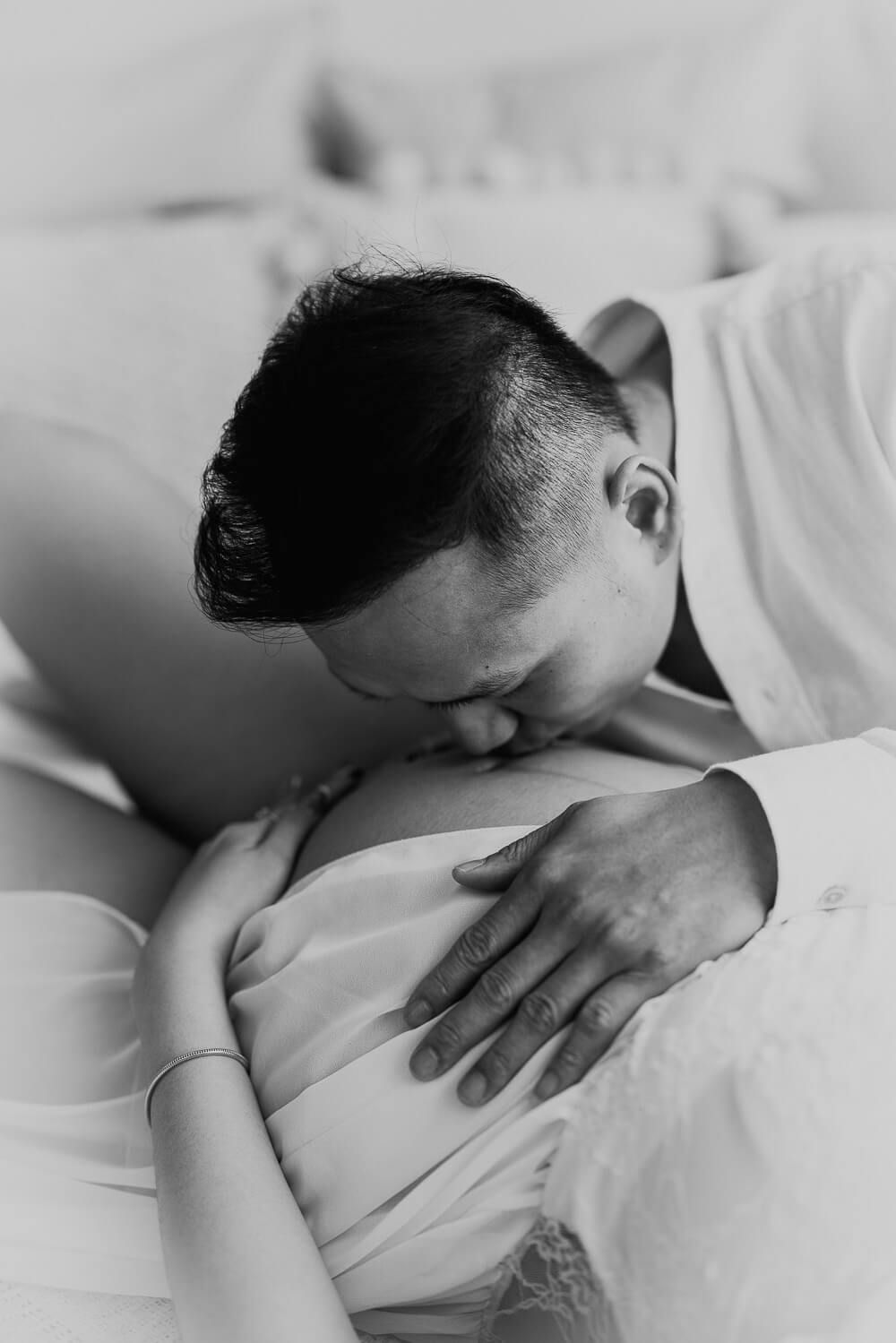 Partner küsst liebevoll den Babybauch seiner schwangeren Frau bei einem emotionalen Schwangerschafts Fotoshooting
