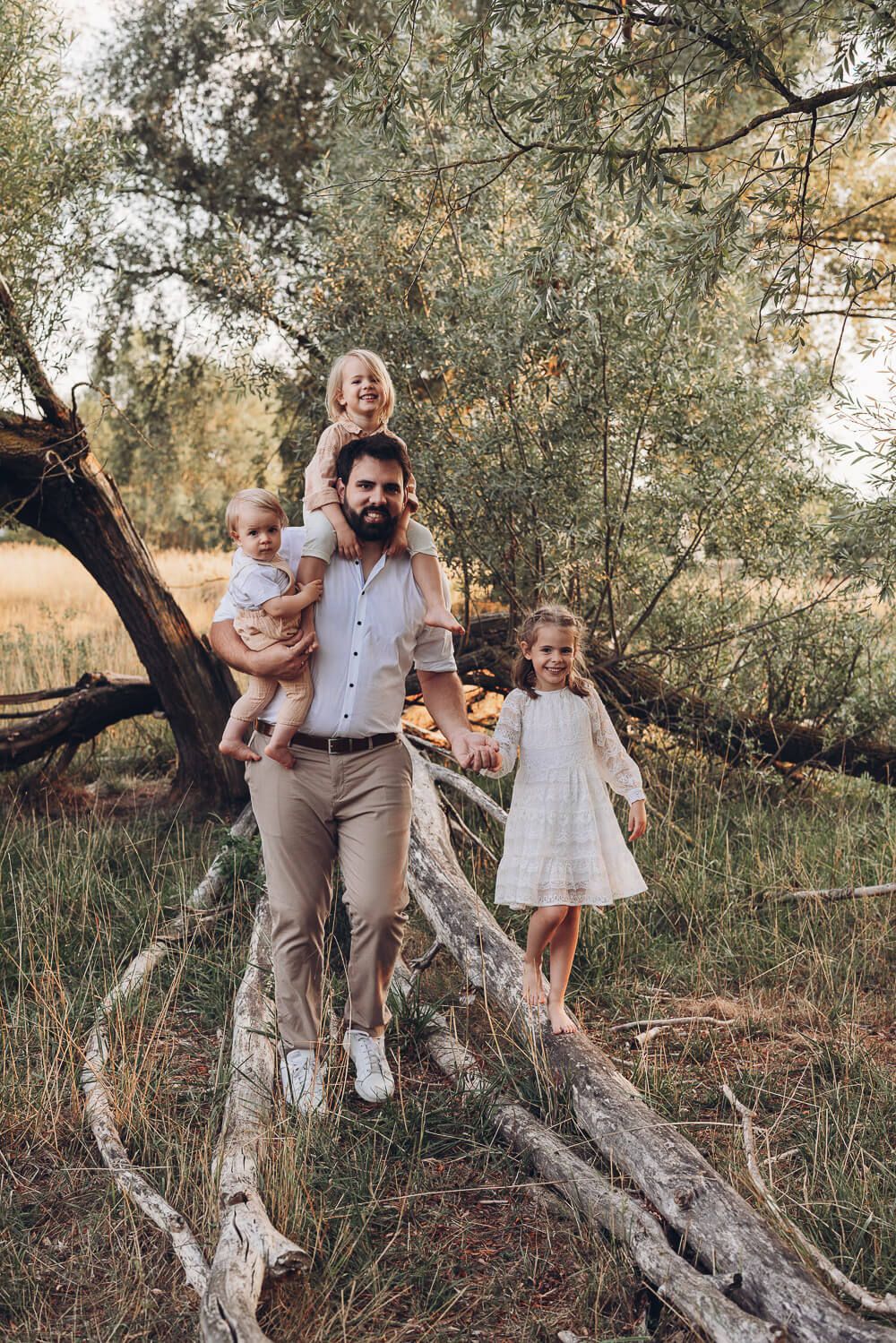 Entspanntes Familienbild beim Outdoorfotoshooting Pattensen, Vater trägt ein Kind und läuft mit seinen Kindern durch den Wald