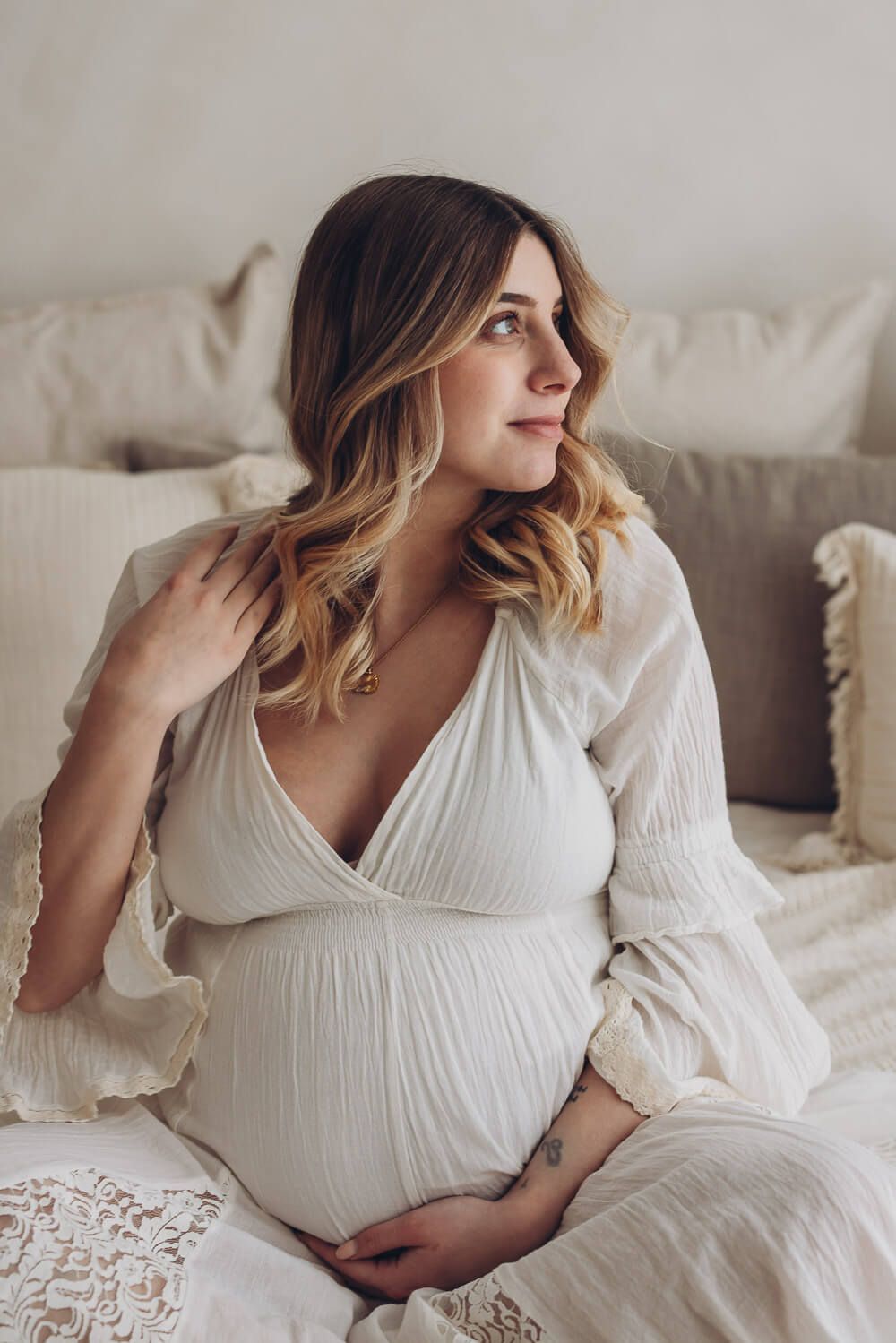 Natürliches Babybauch Fotoshooting im Fotostudio in Langenhagen – werdende Mutter sitzt entspannt auf einem Bett