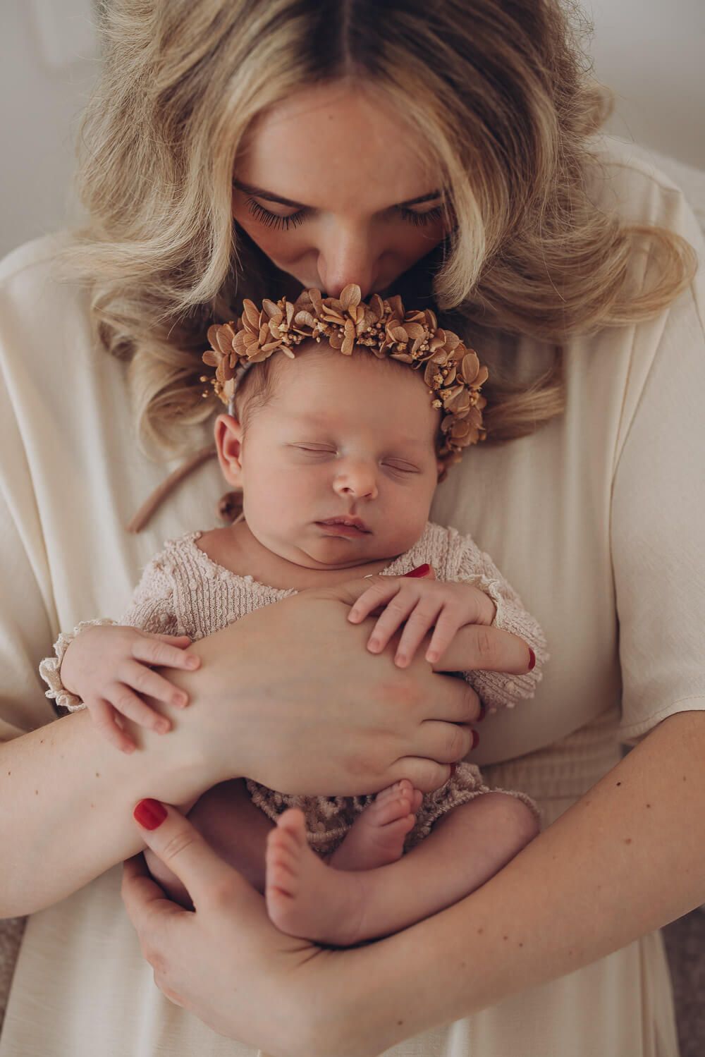 Emotionale Newborn Fotografie in Braunschweig – Mutter küsst ihr schlafendes Baby mit Blumenkranz liebevoll auf den Kopf