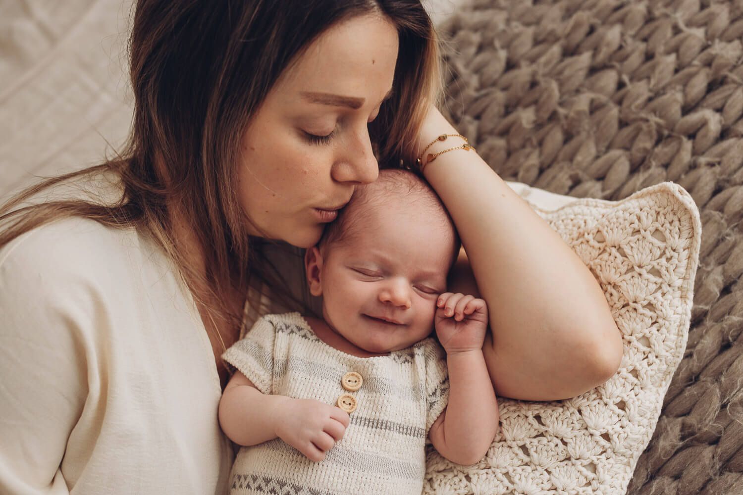 Mutter küsst ihr Baby, das dabei leicht lächelt – emotionales Newborn Fotoshooting in Hannover