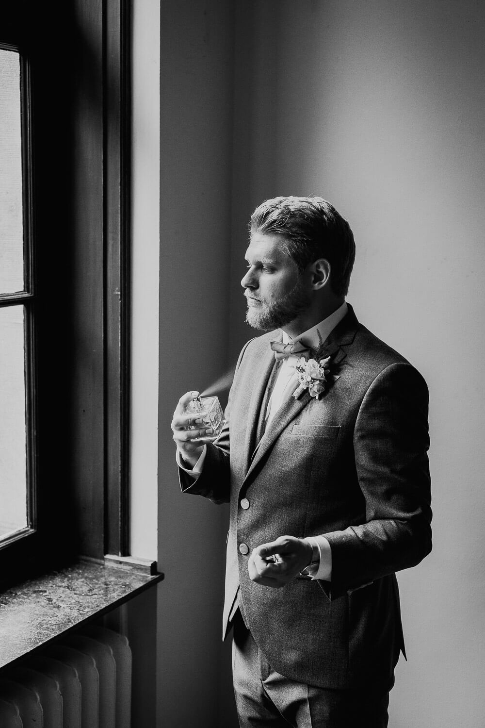 Stilvolle Schwarz-Weiß-Aufnahme des Bräutigams am Fenster mit Glas in der Hand, festgehalten von einem Hochzeitsfotografen in Hildesheim