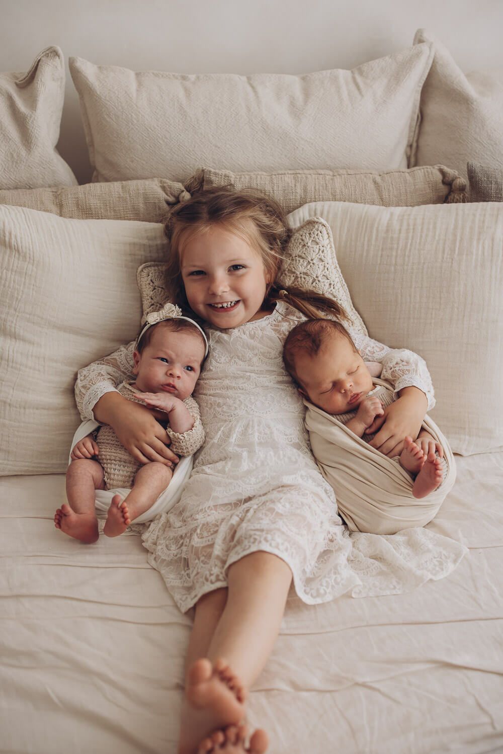 Süßes Geschwisterbild im Fotostudio in Sehnde – großes Mädchen liegt mit zwei neugeborenen Babys auf dem Sofa