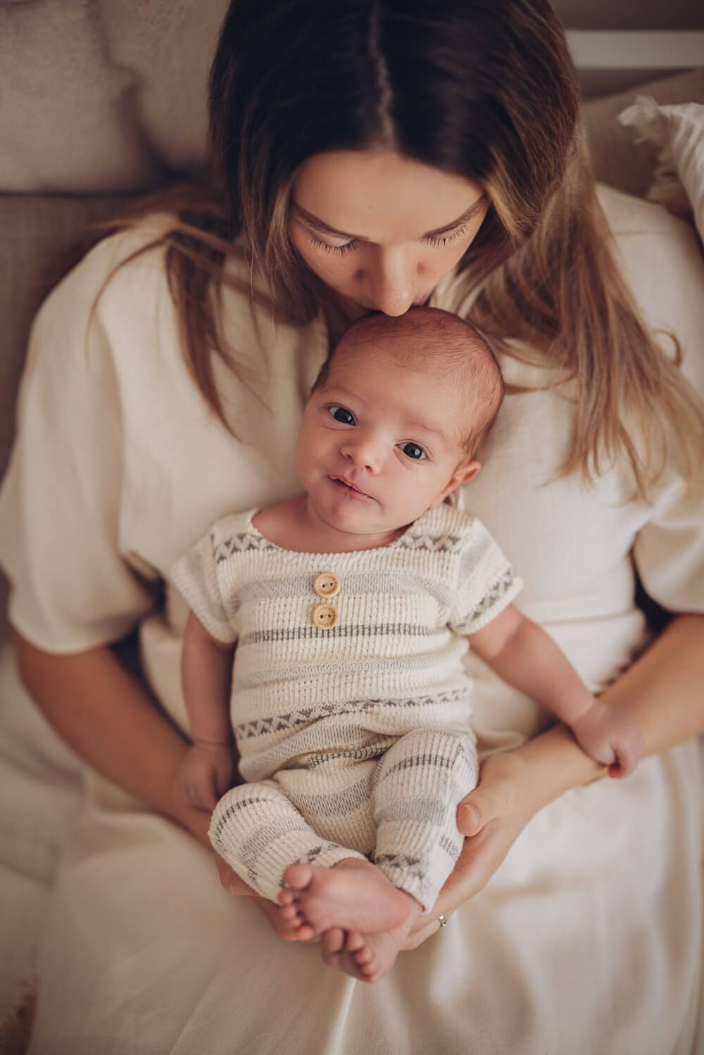 Baby schaut in die Kamera während die Mutter es liebevoll auf den Kopf küsst