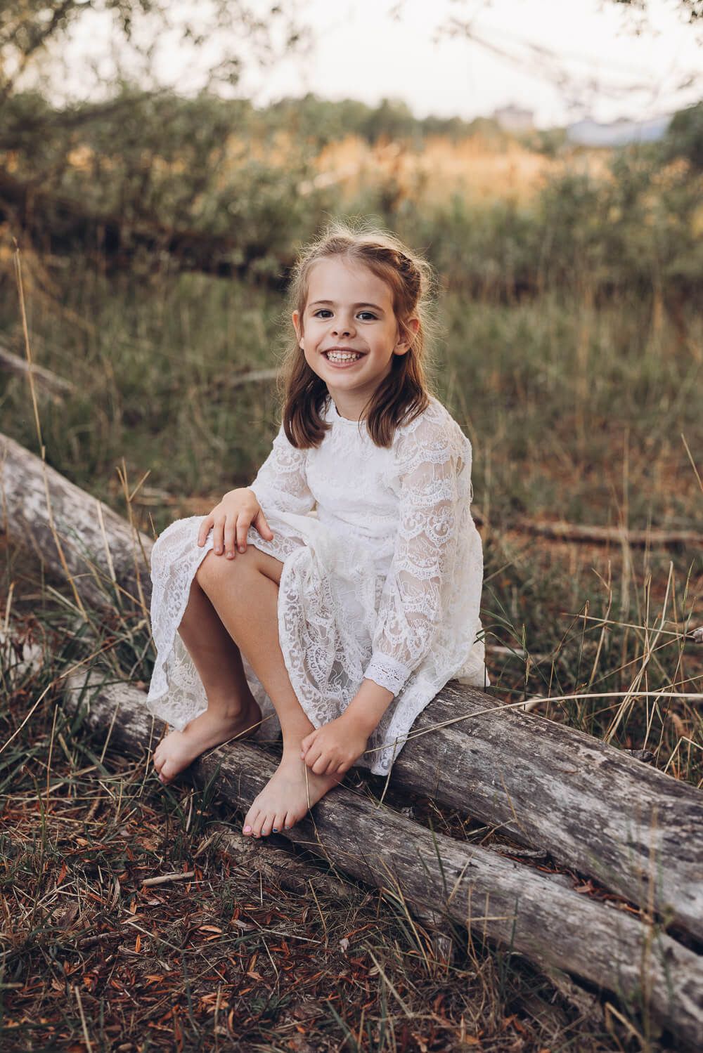 Natürliches Kinderportrait beim Outdoorfotoshooting Barsinghausen, Mädchen sitzt auf einem Baumstamm und lächelt in die Kamera