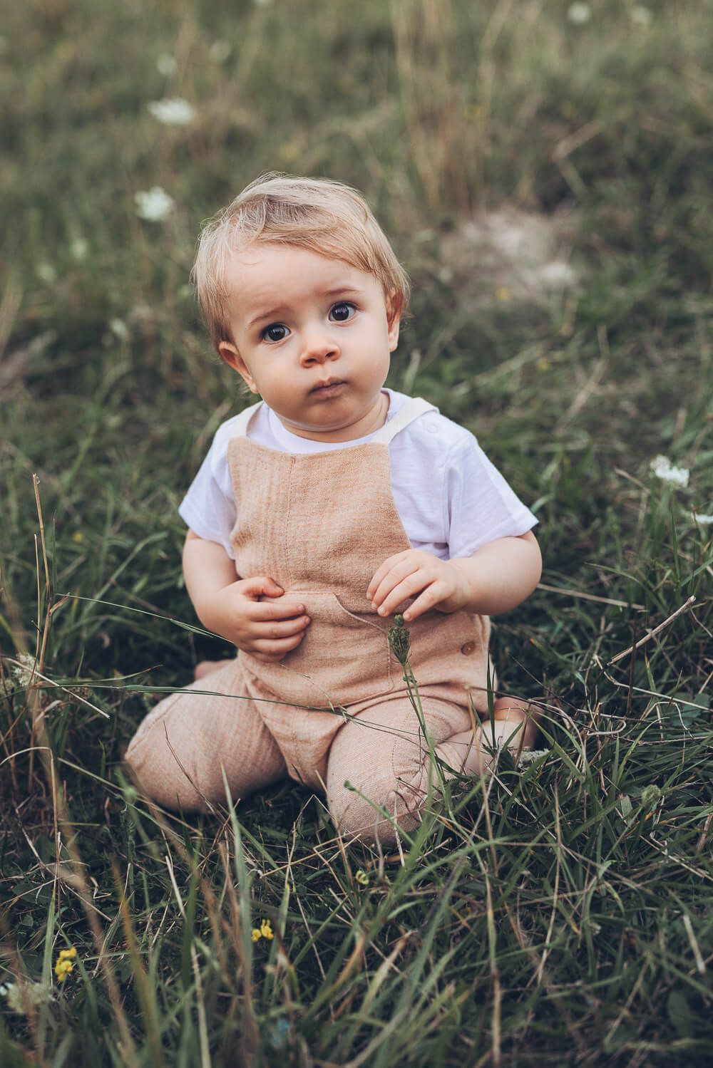 Natürliches Baby sitzt neugierig im Gras beim Outdoor Shooting Hannover und schaut aufmerksam in die Umgebung
