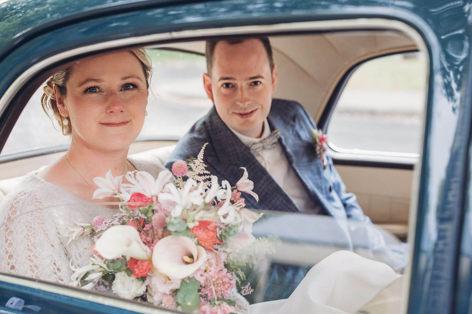 Brautpaar sitzt mit Blumenstrauß in einem blauen Oldtimer während einer Hochzeit in Hannover