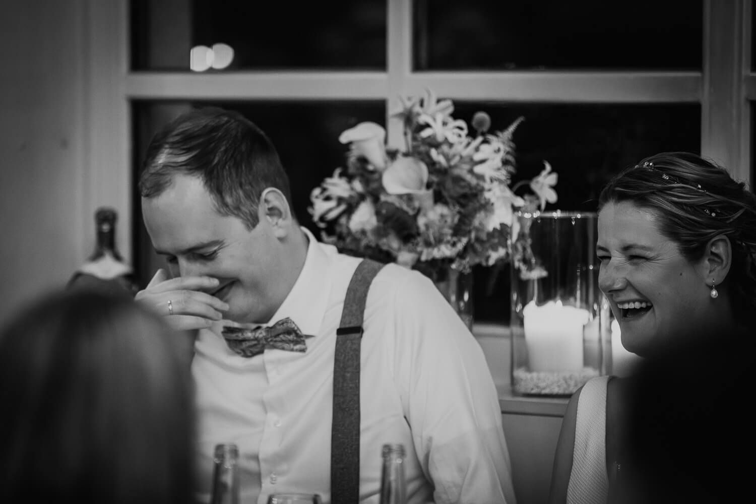 Braut und Bräutigam lachen herzlich während der Feier am Tisch, ungestellt festgehalten in einer Hochzeitsreportage aus Hannover