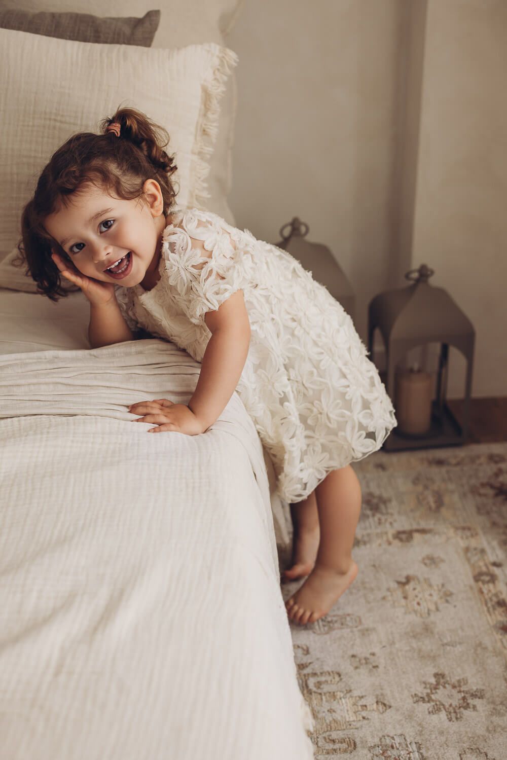Fröhliches Kleinkindmädchen lehnt sich lächelnd an ein Bett bei einem Fotoshooting in Wolfsburg