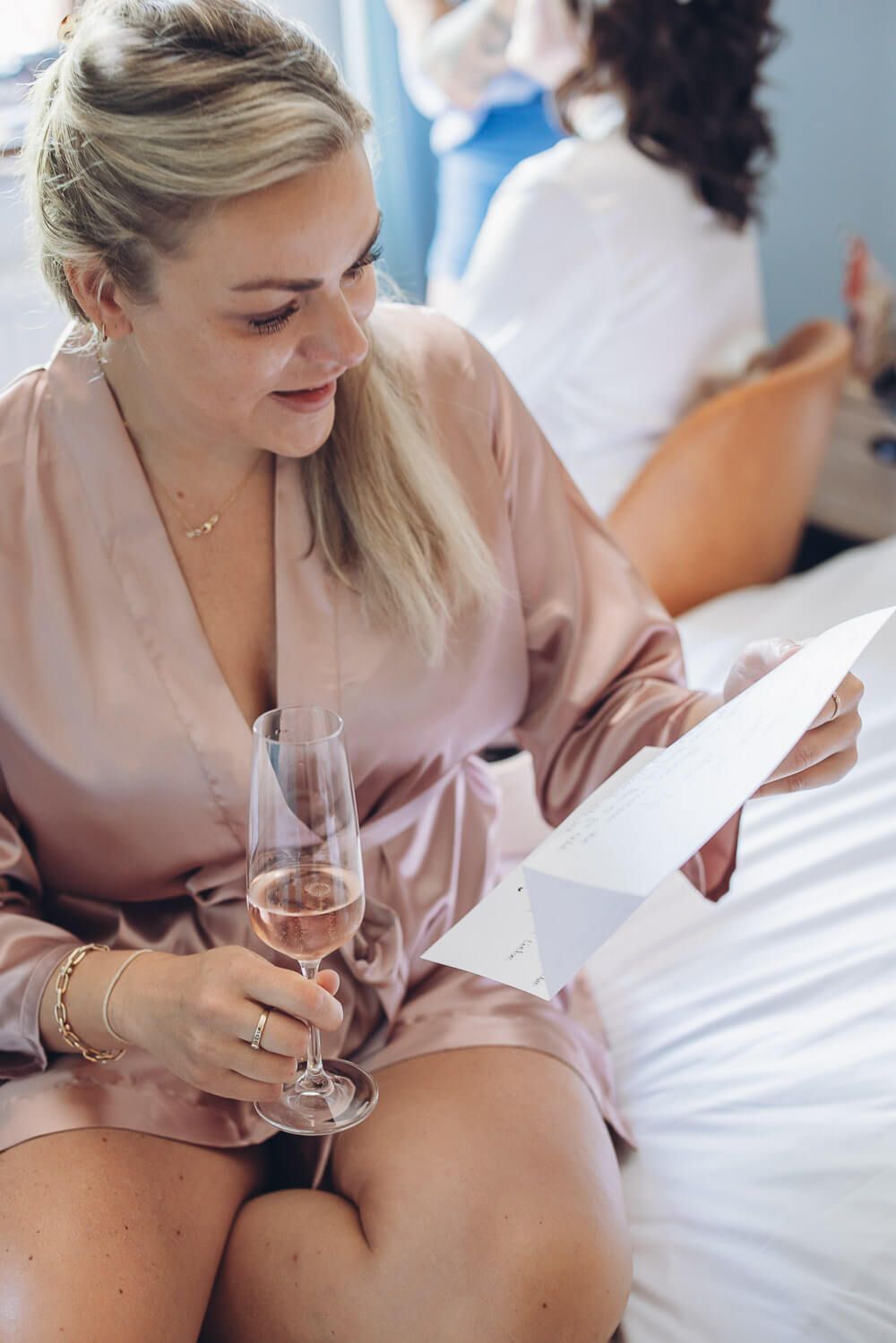 Brautjungfer im Morgenmantel liest gerührt einen persönlichen Brief und hält ein Glas Sekt beim Getting Ready für eine freie Trauung - Foto