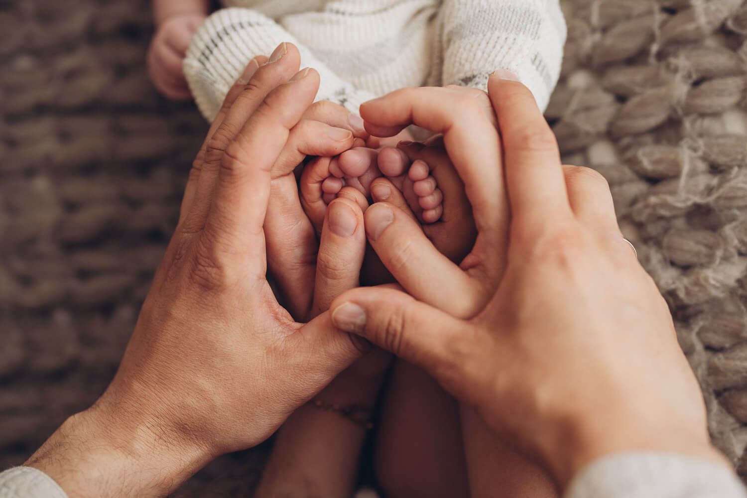 Eltern formen mit ihren Händen ein Herz um die kleinen Füße ihres Babys