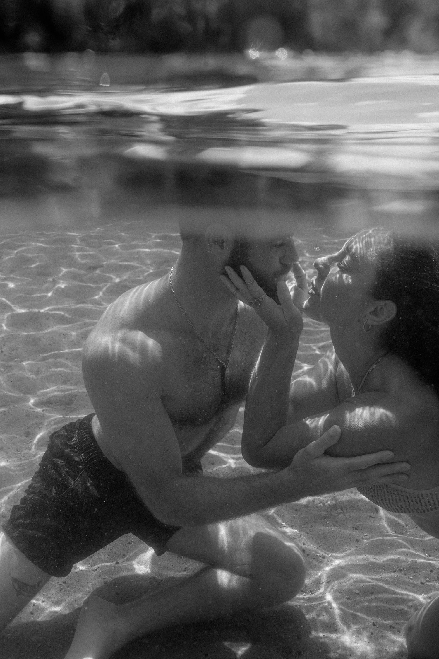 A romantic black and white underwater photograph showing an intimate moment in a swimming pool.