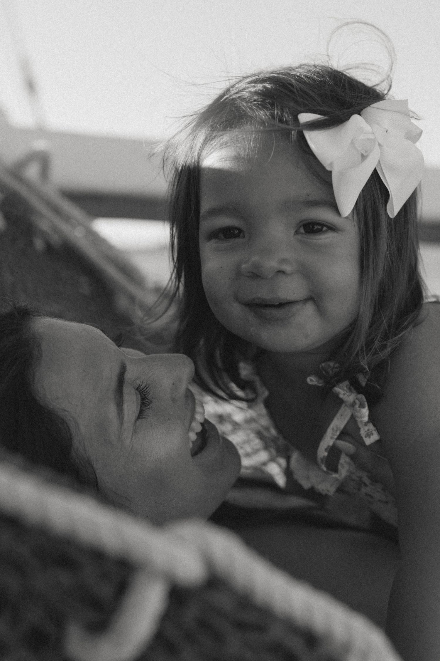 Black and white photo of a smiling toddler girl with a white bow in her hair being held by a woman.