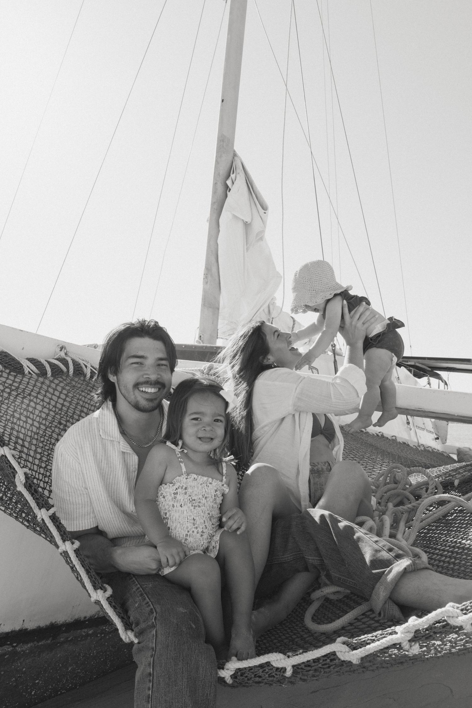 Black and white photo of a happy family relaxing on a sailboat deck, parents smiling with two young children.