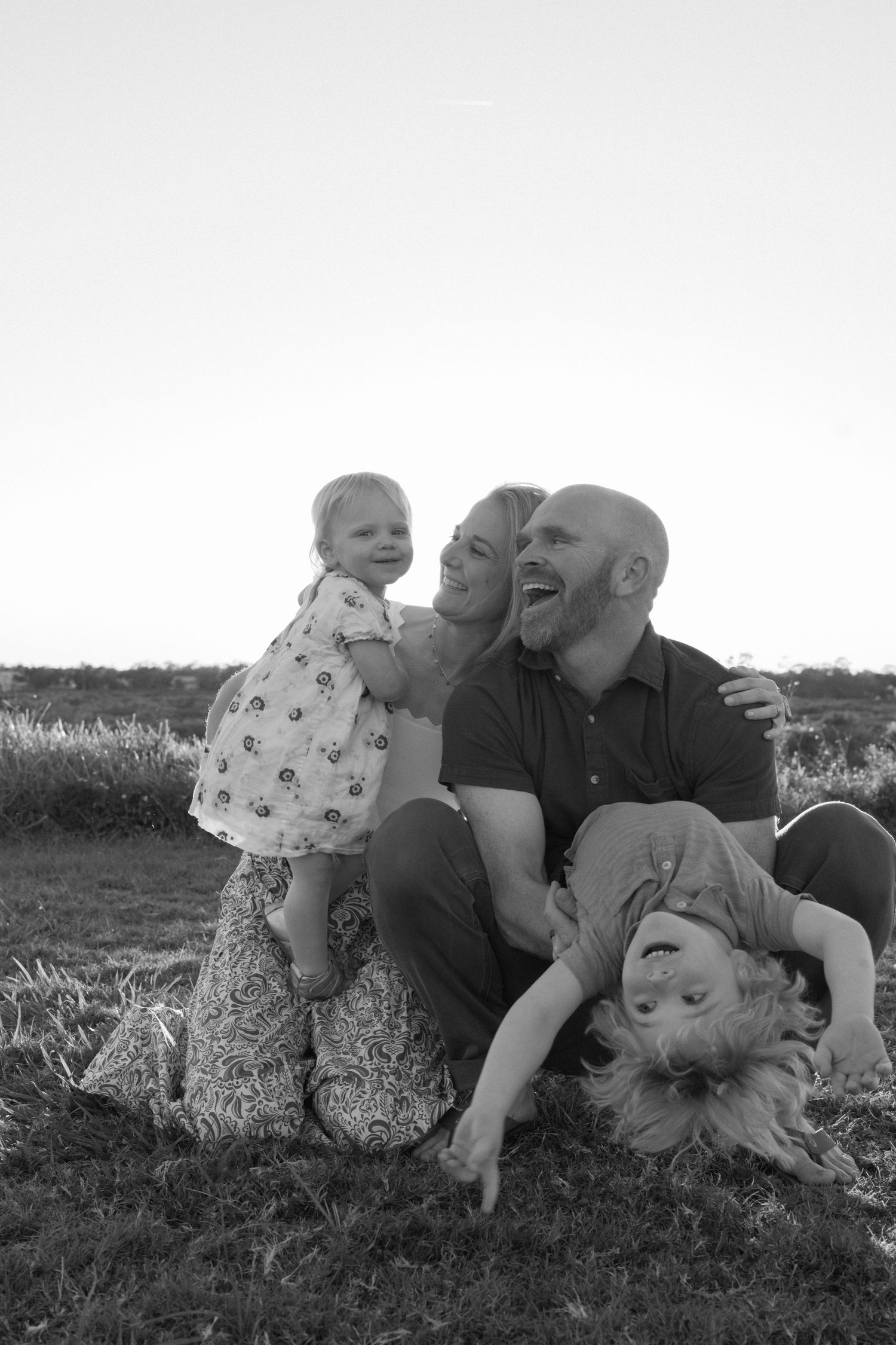 A joyful black and white family portrait showing playful interaction outdoors on grassy ground.