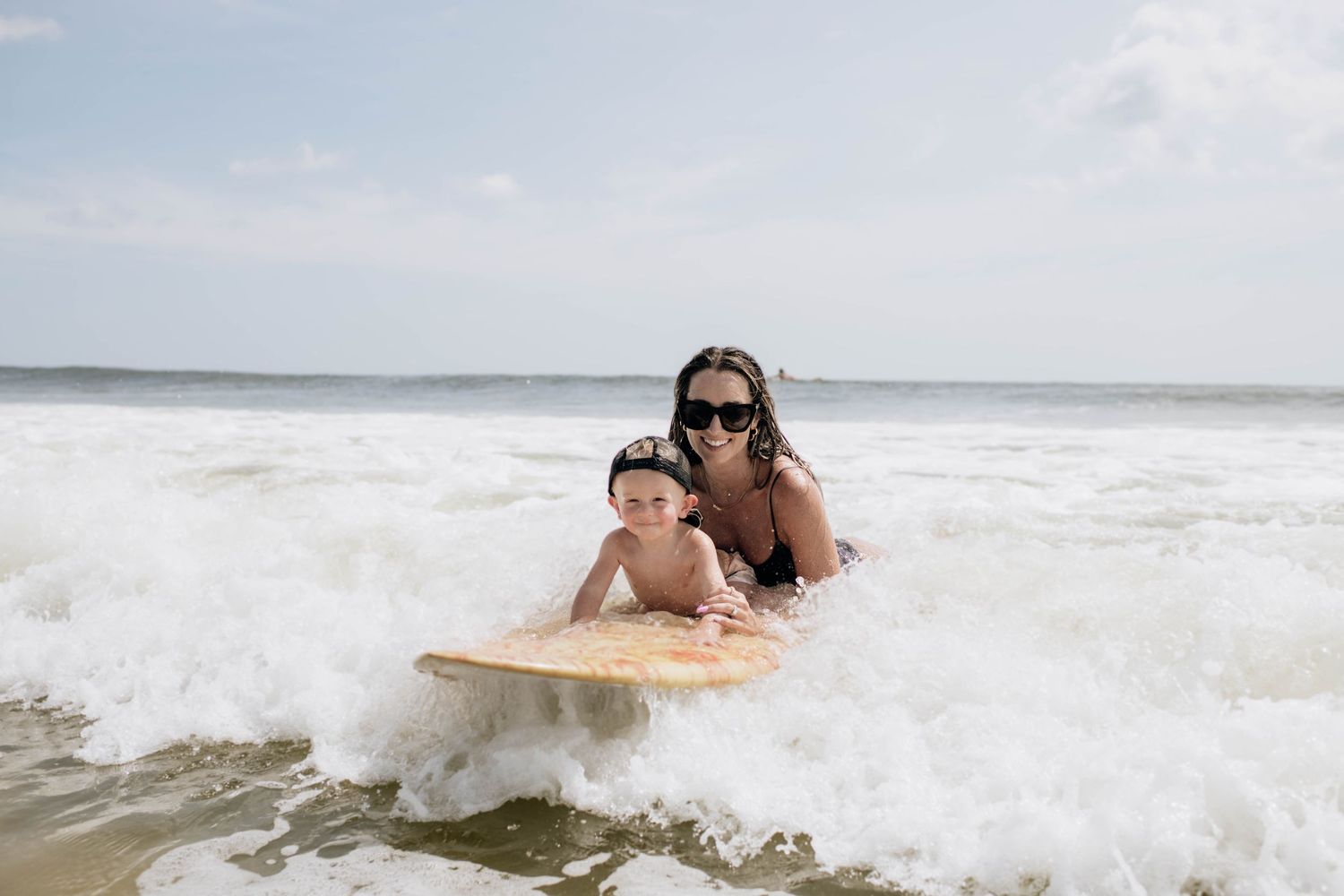 A surfer in black swimwear rides a wave through foamy white ocean water on a wooden surfboard.