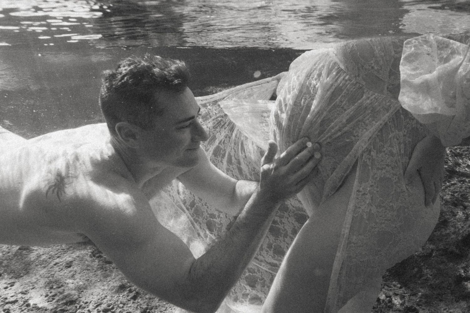 Black and white underwater photo of a couple sharing a romantic moment beneath the surface.