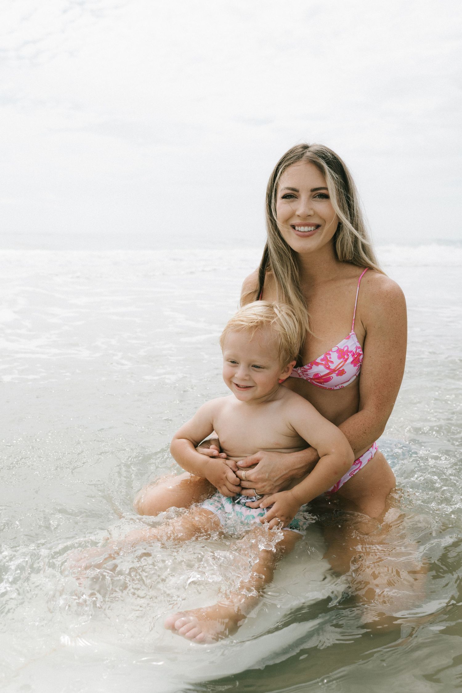A parent and baby play together in the ocean waves on a bright summer day at the beach.