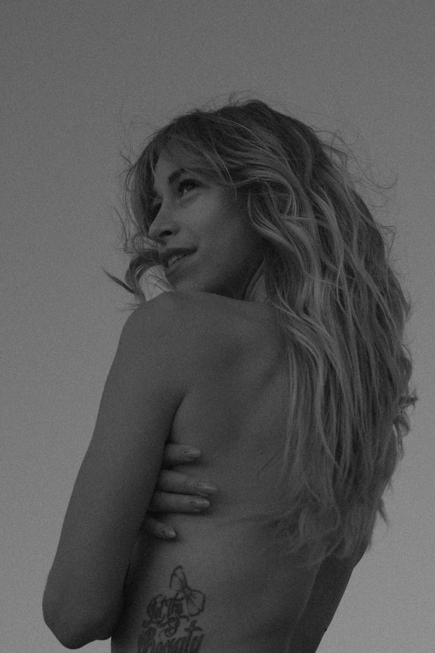 Black and white artistic portrait of long wavy hair and a visible butterfly tattoo on bare back.