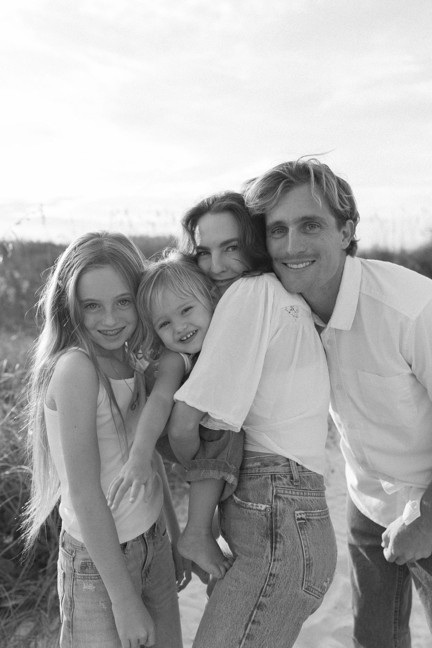 A series of black and white candid photos showing a casual family group embracing and laughing together outdoors.