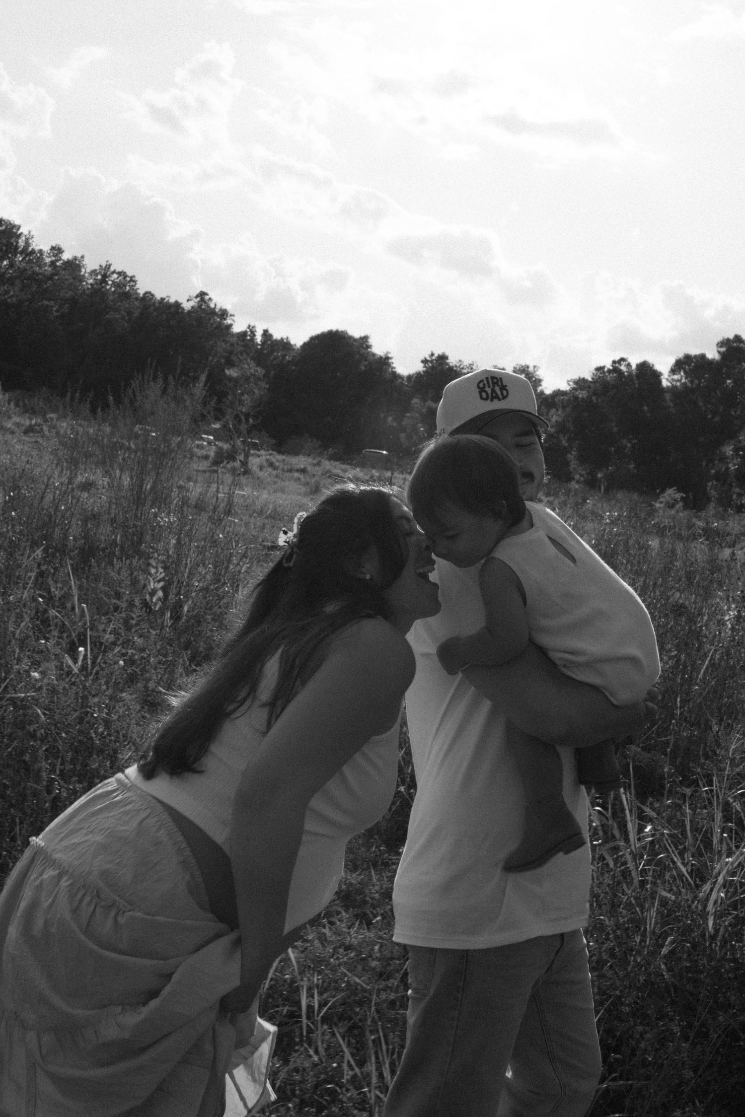 Black and white photo of a couple in a meadow with trees in the background during golden hour.