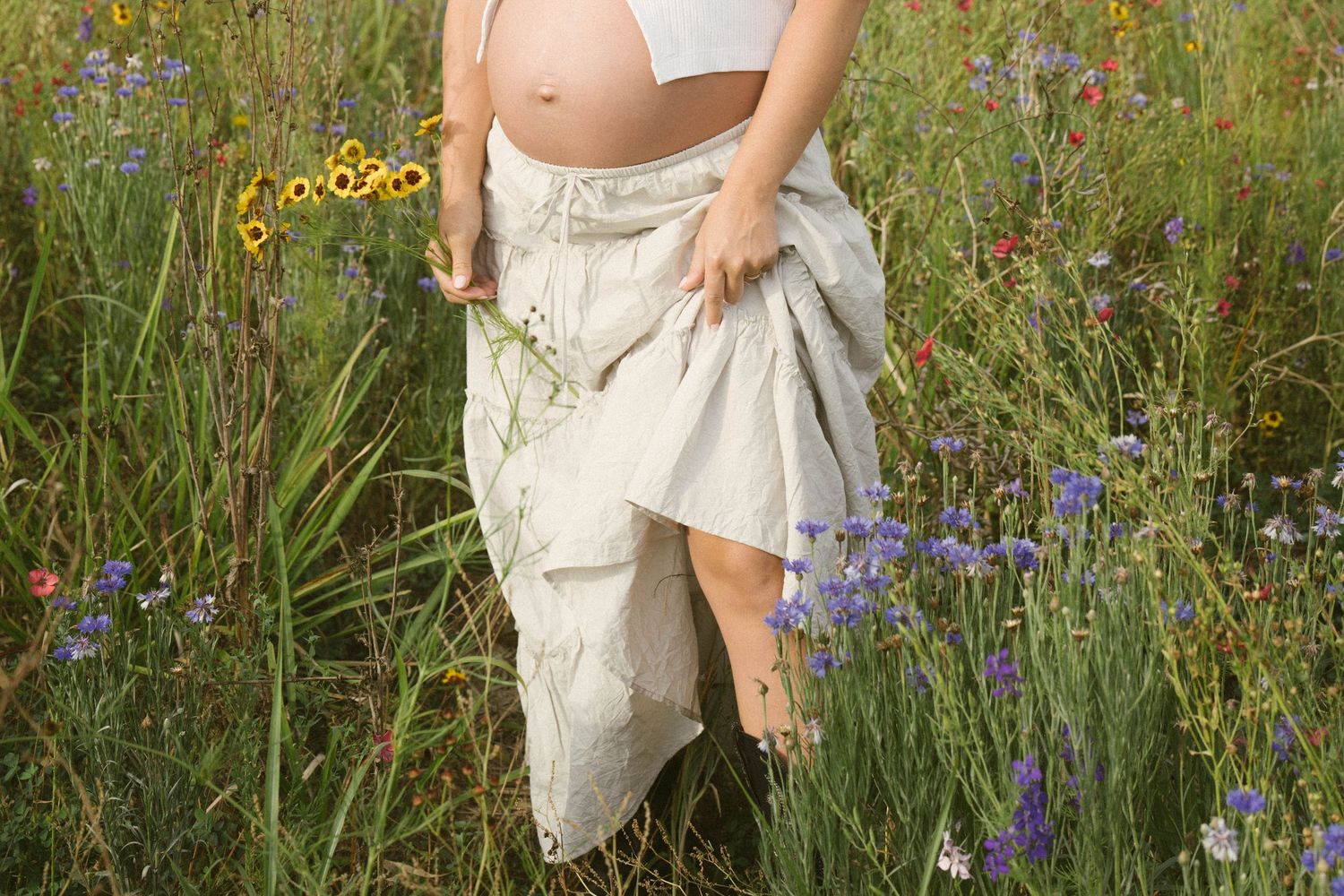 Someone wearing a white flowy dress stands in a wildflower meadow with purple and yellow blooms.