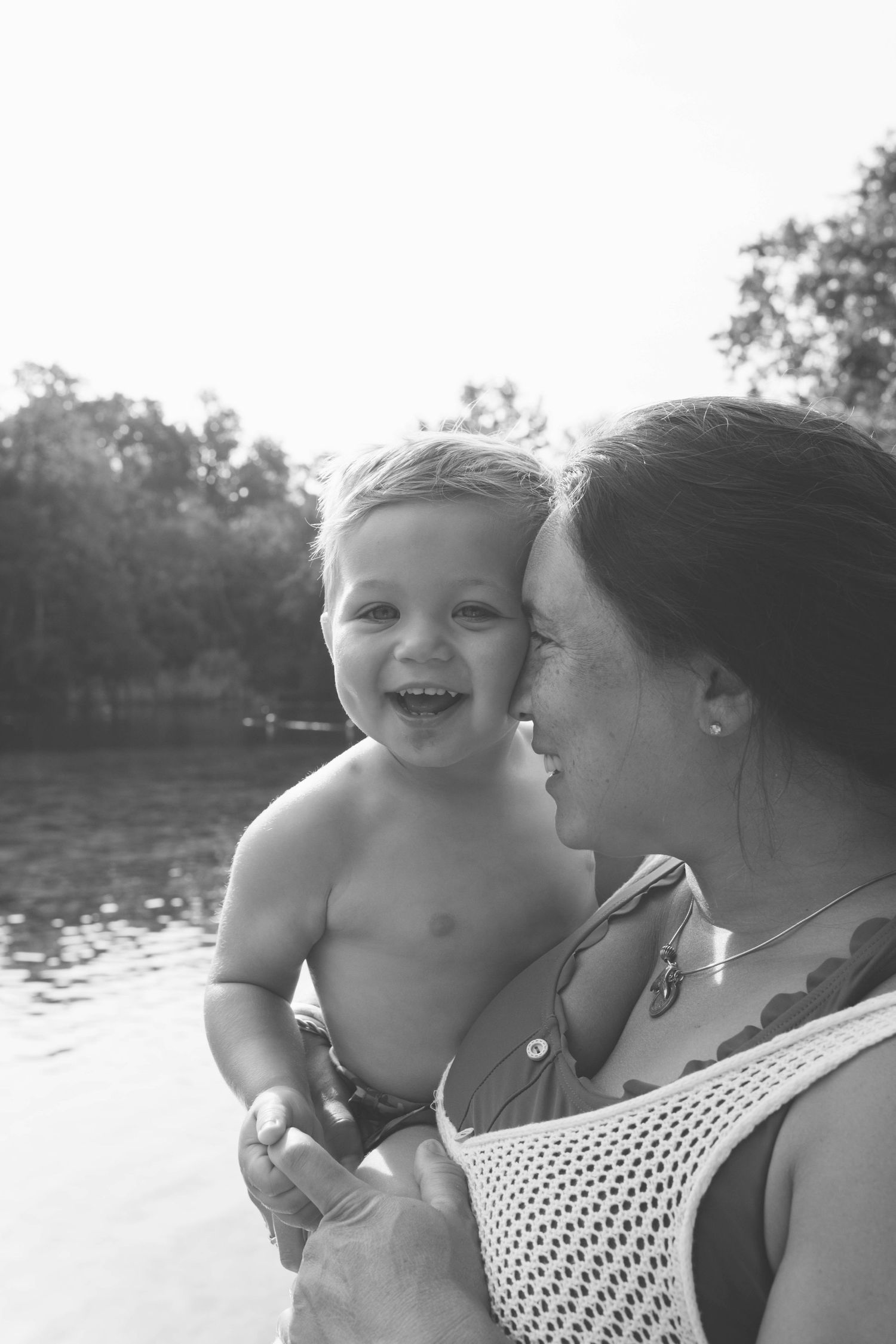 A joyful candid black and white photo capturing a tender moment by the water on a sunny day.