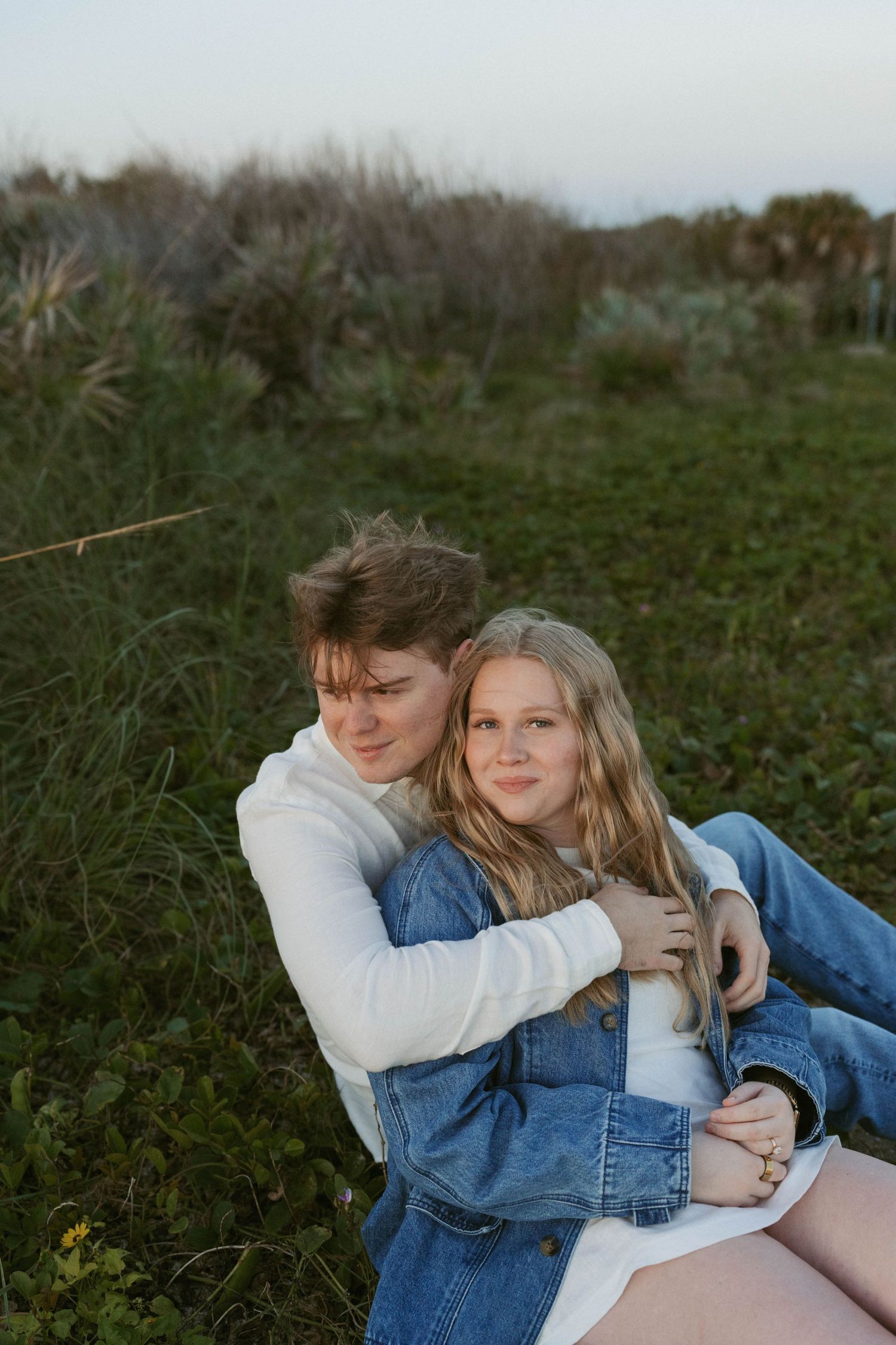 Two teenagers sitting together in a grassy field, sharing a warm embrace at golden hour.