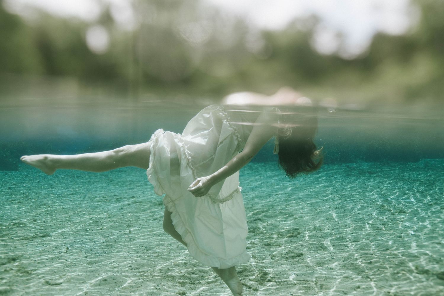 Ethereal underwater photograph of a figure in white dress floating gracefully beneath the turquoise surface.