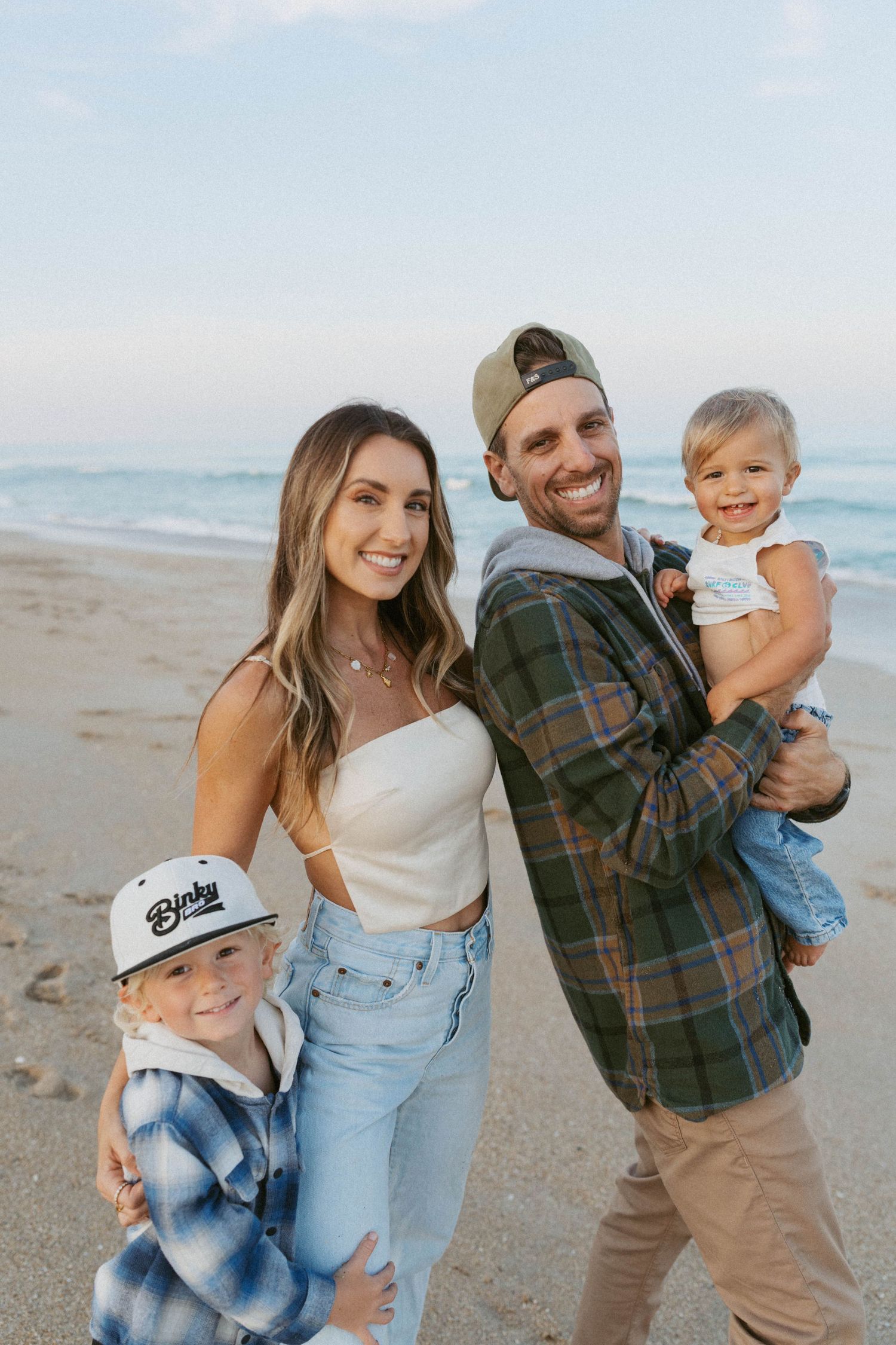 A family enjoys a sunny day together on the beach with ocean waves in the background.