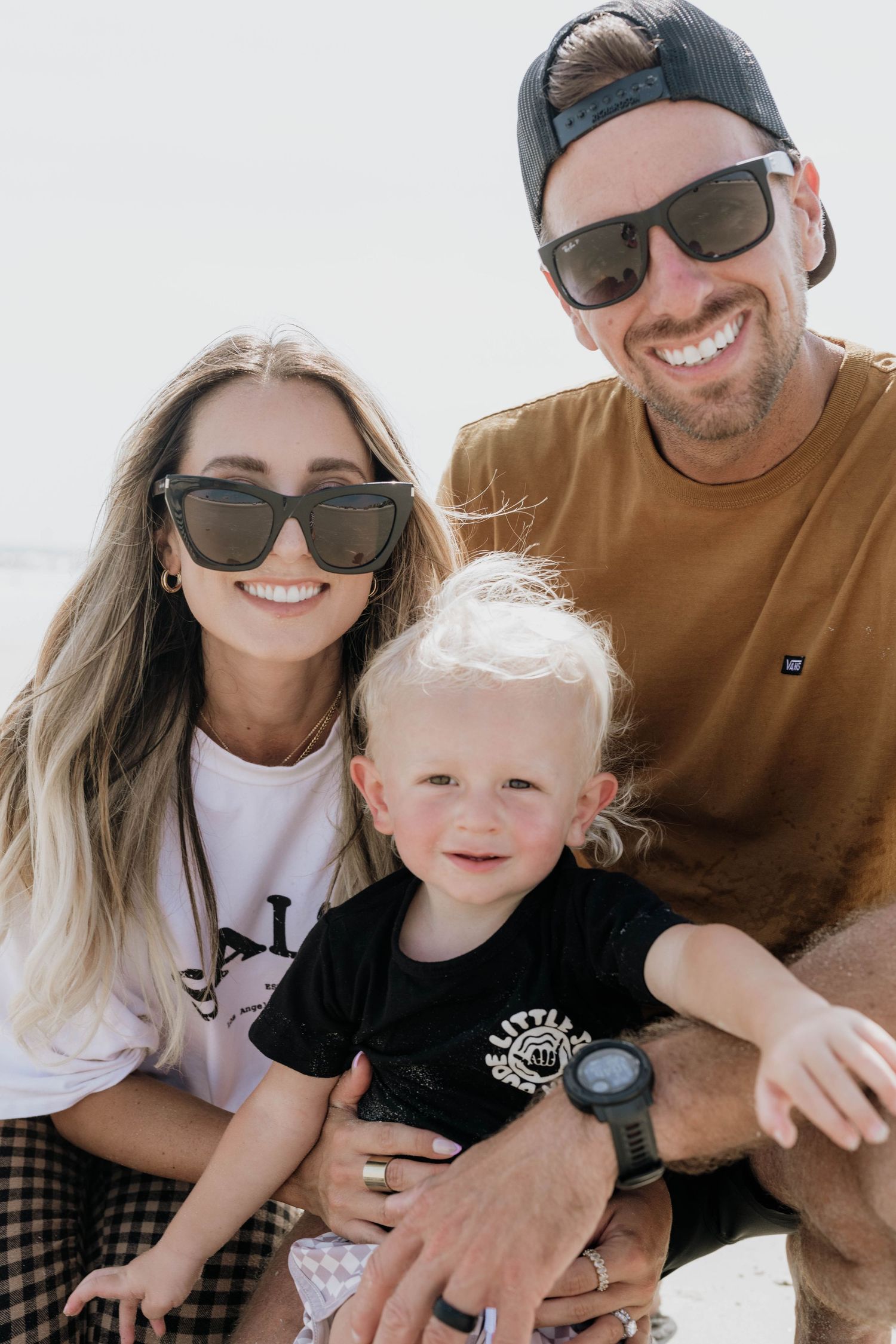 Family wearing sunglasses smiles together outside on a bright sunny day.