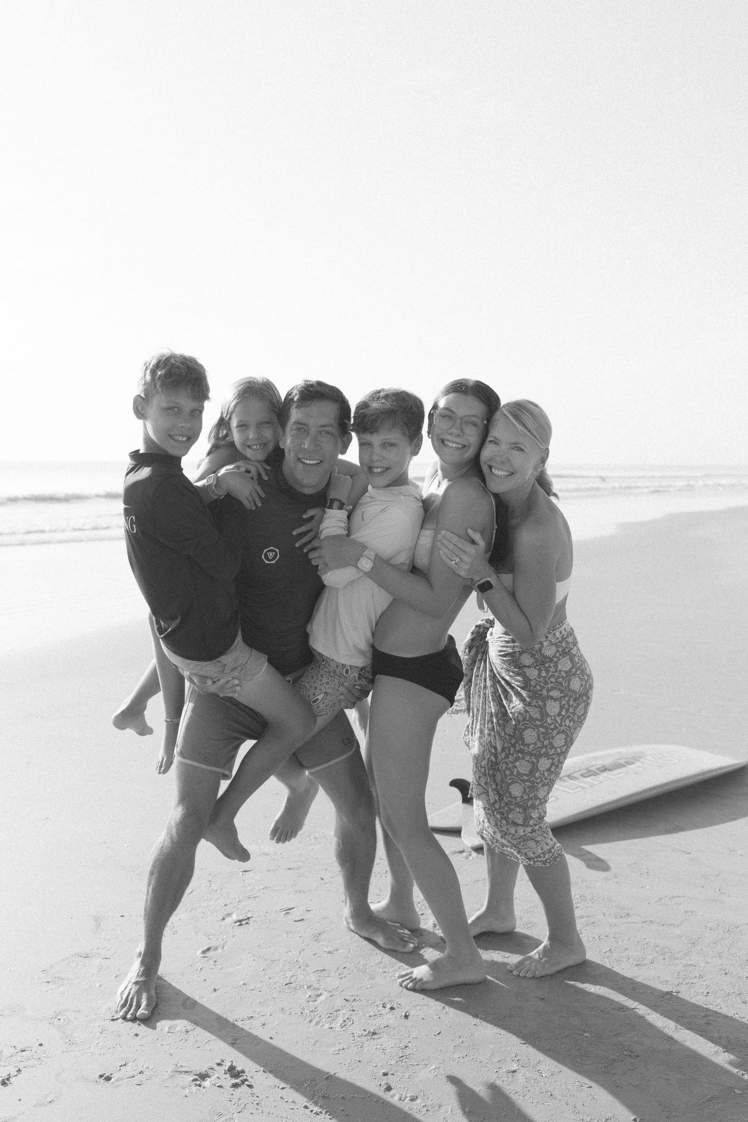 A group of friends pose playfully together on a sunny beach in black and white photography.