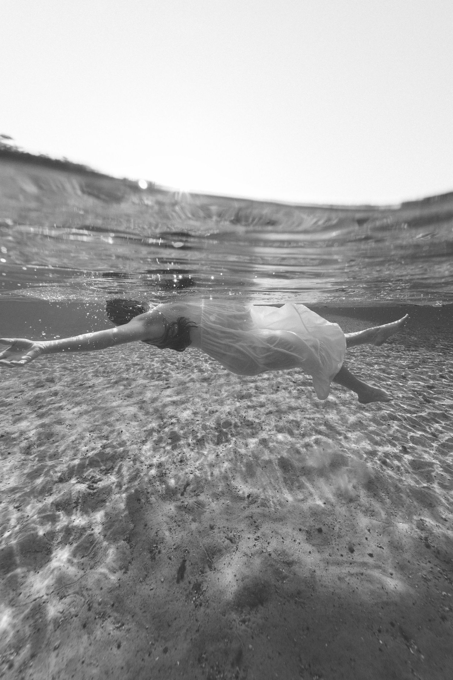 Black and white underwater photograph showing a graceful silhouette floating near the sandy ocean floor.