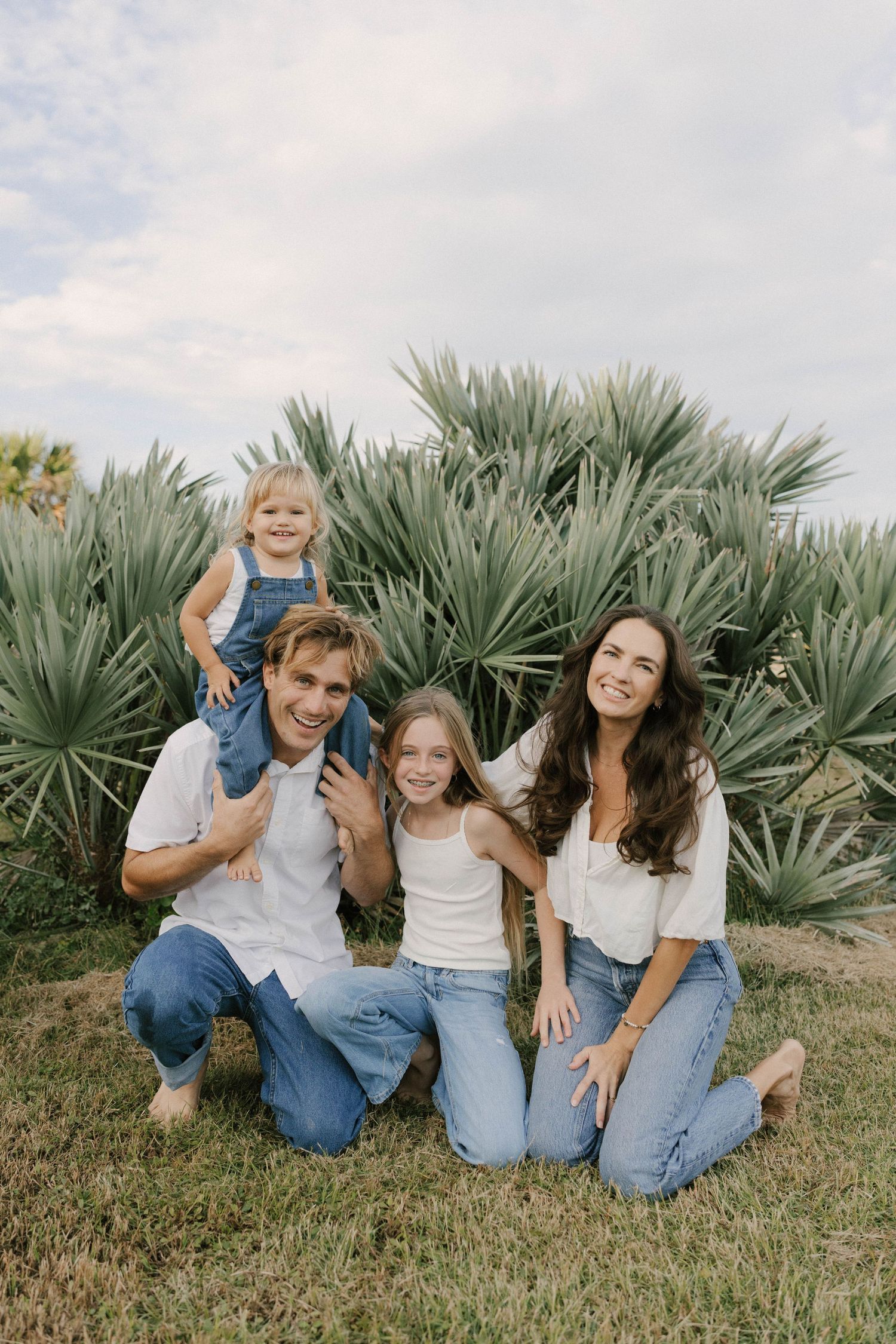 A group sits together on grass in front of agave plants, wearing matching denim and white outfits in a casual outdoor setting.