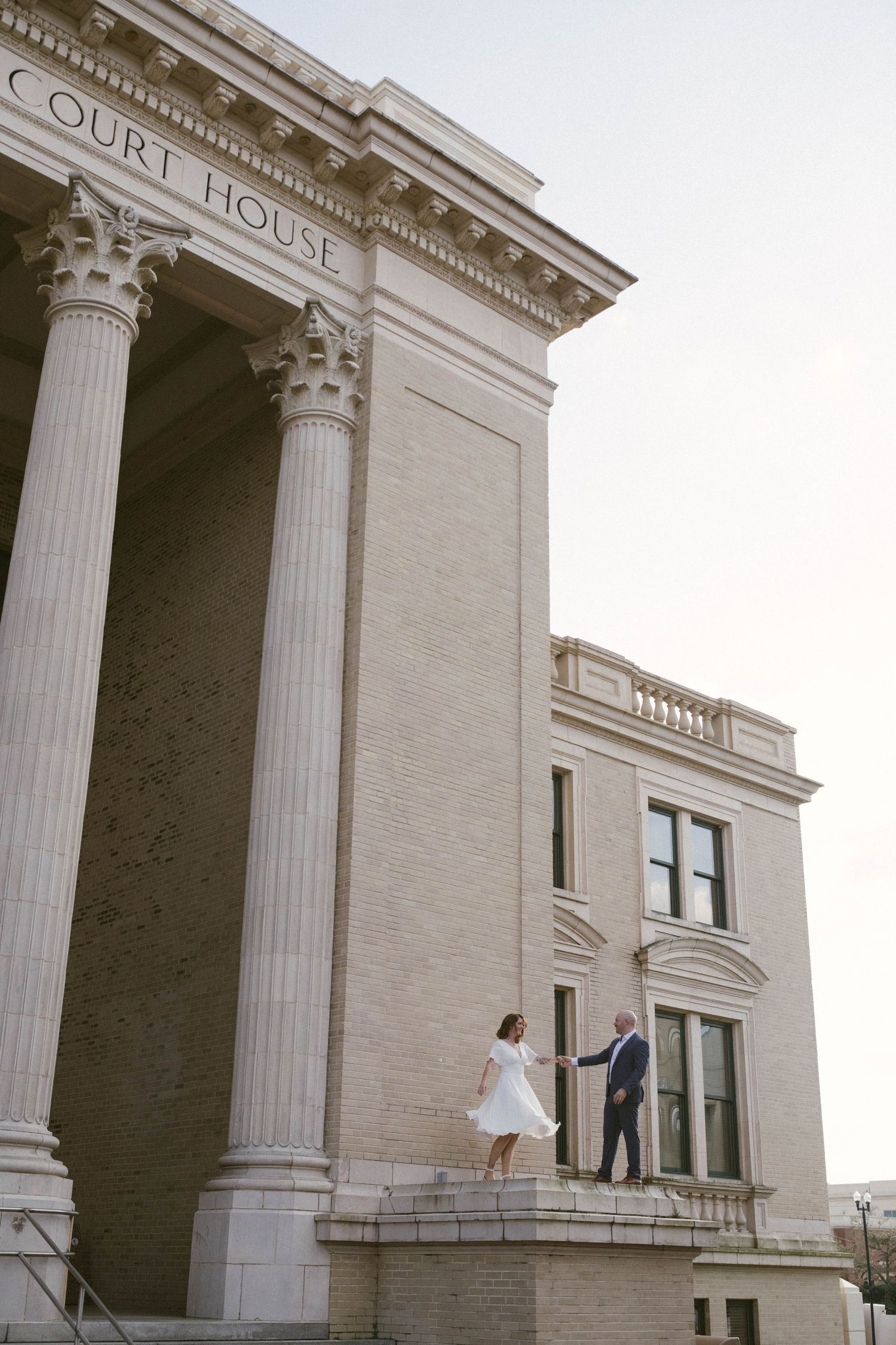 A white neoclassical building exterior with tall Corinthian columns and two people visible in the distance.