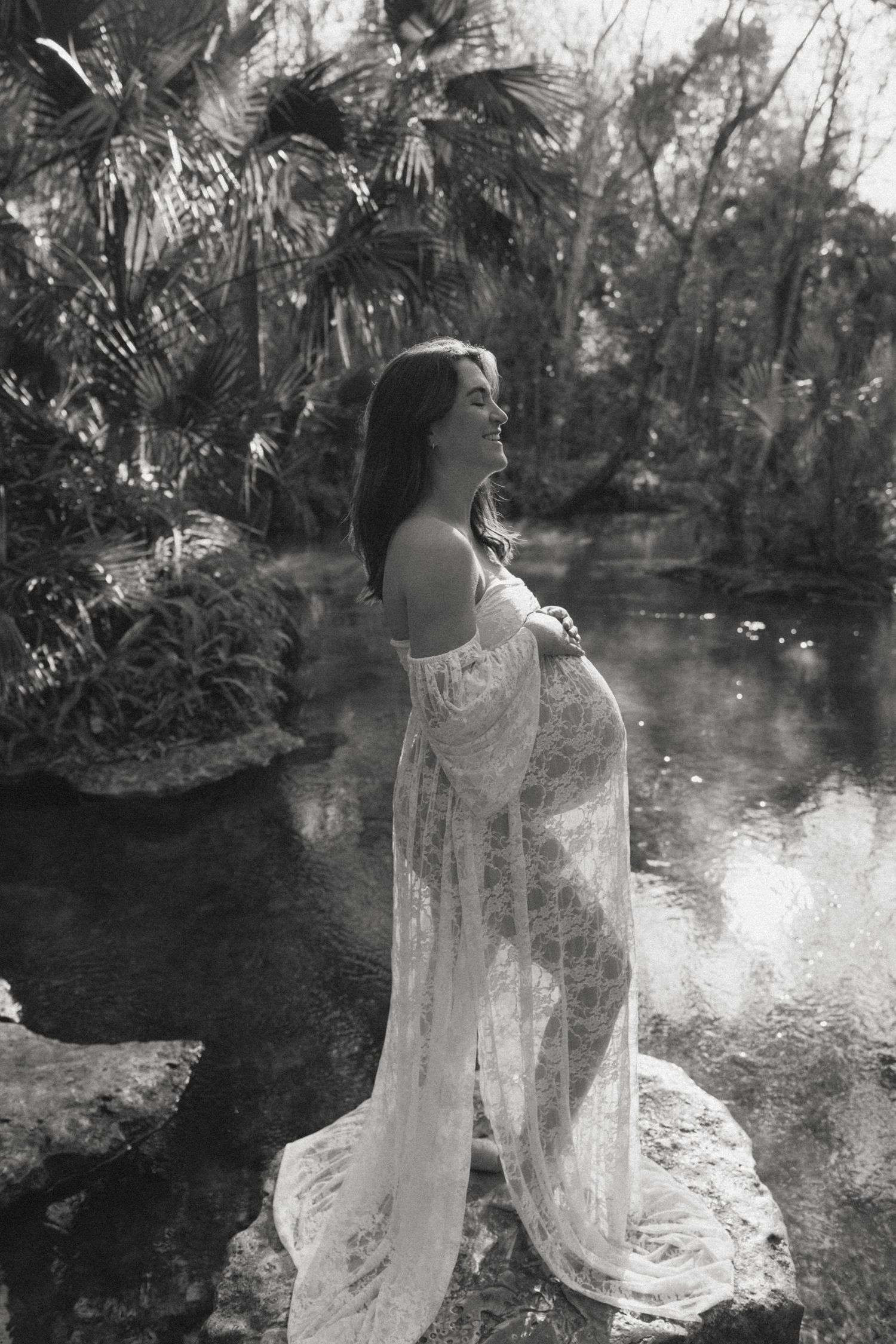 A figure in a flowing white dress stands ethereally by a tranquil pond in a lush garden setting.