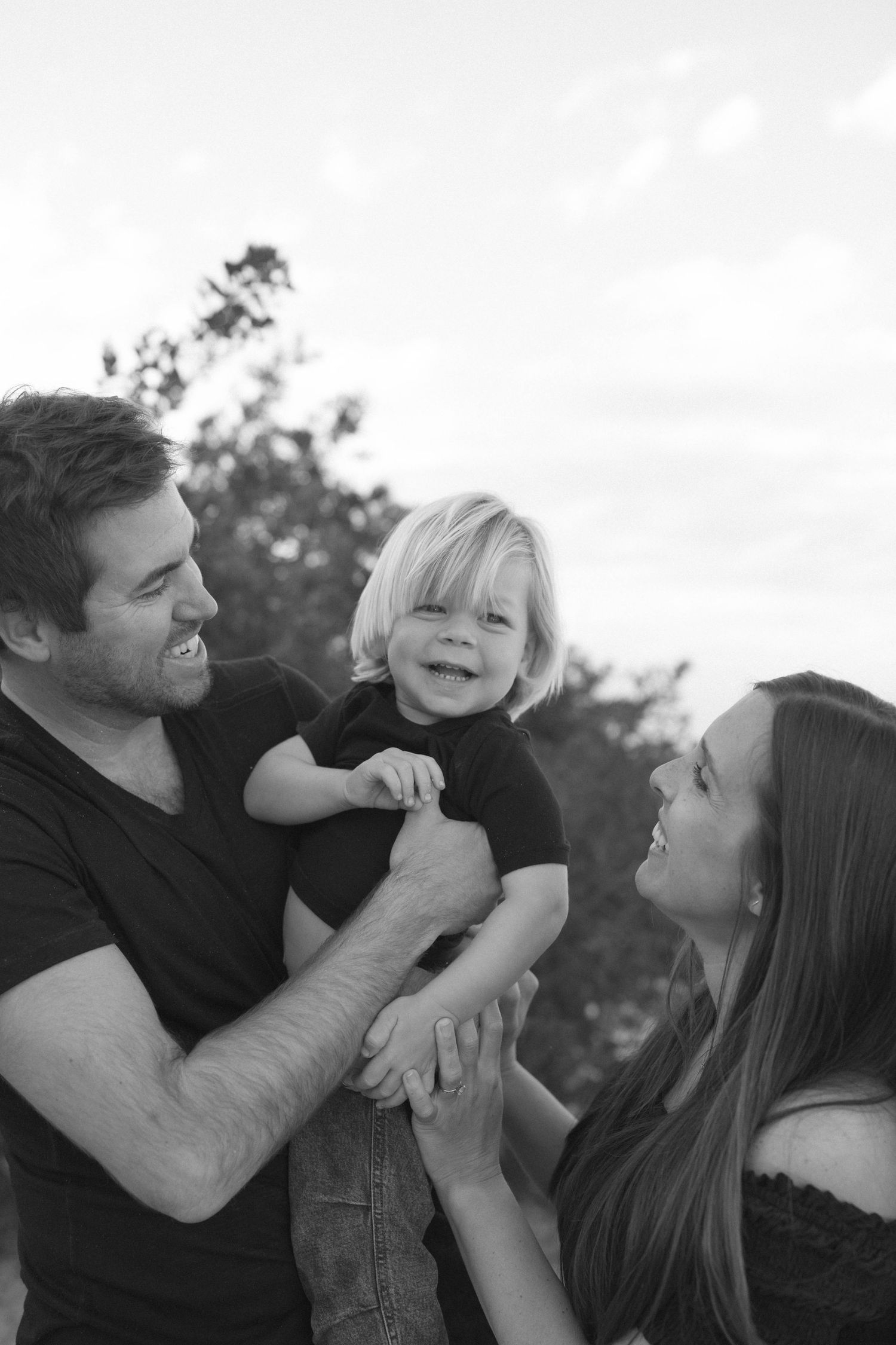 A candid black and white family portrait showing loving interaction outdoors during a casual photo session.
