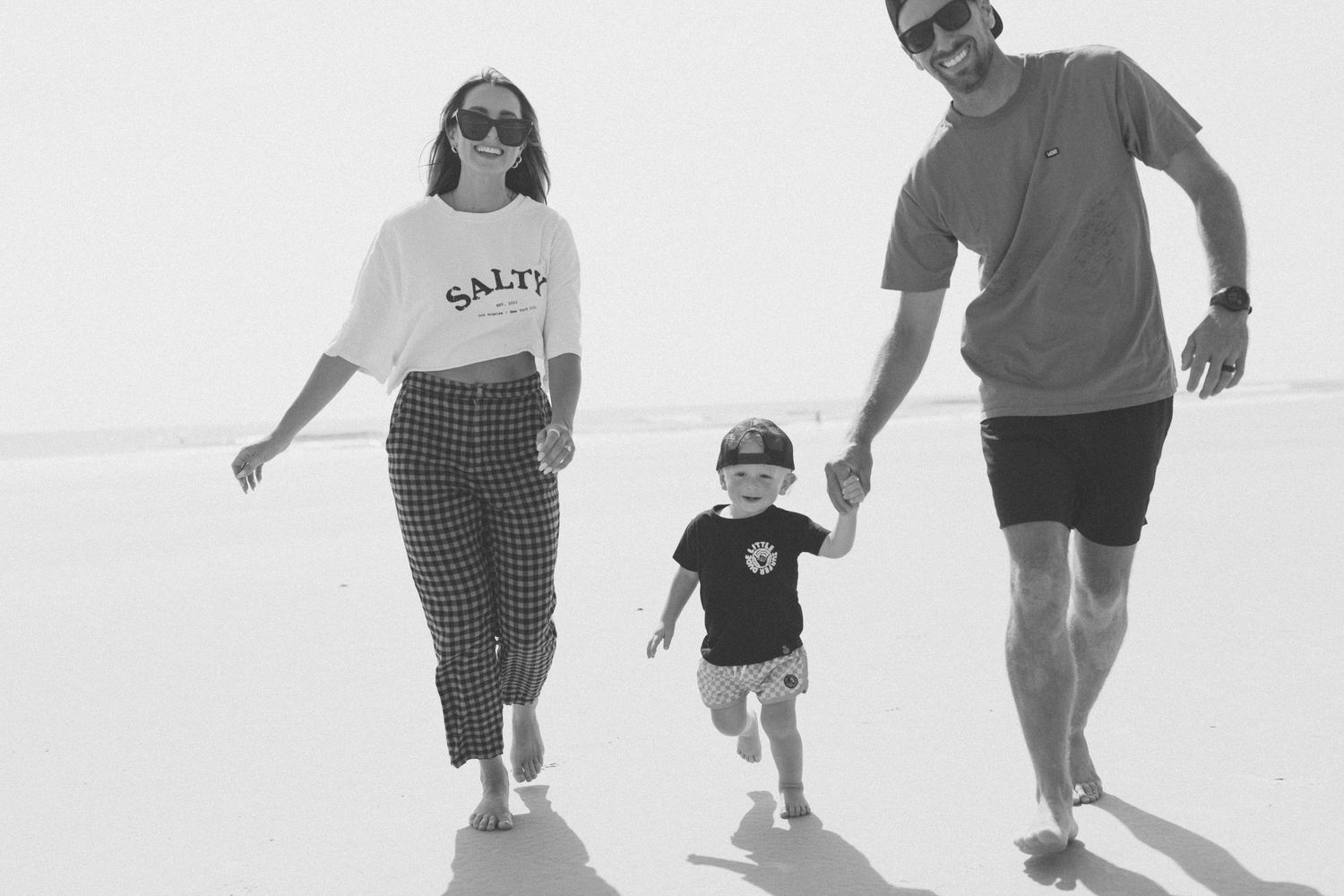 A family in casual attire walking together on a bright white background in black and white photography.
