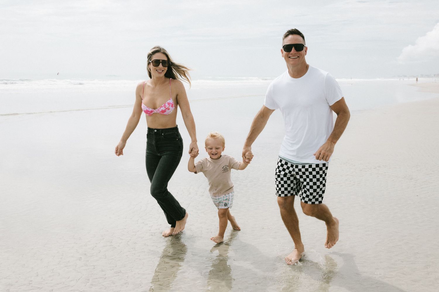 Family holding hands while walking along a white sandy beach with waves in the background.