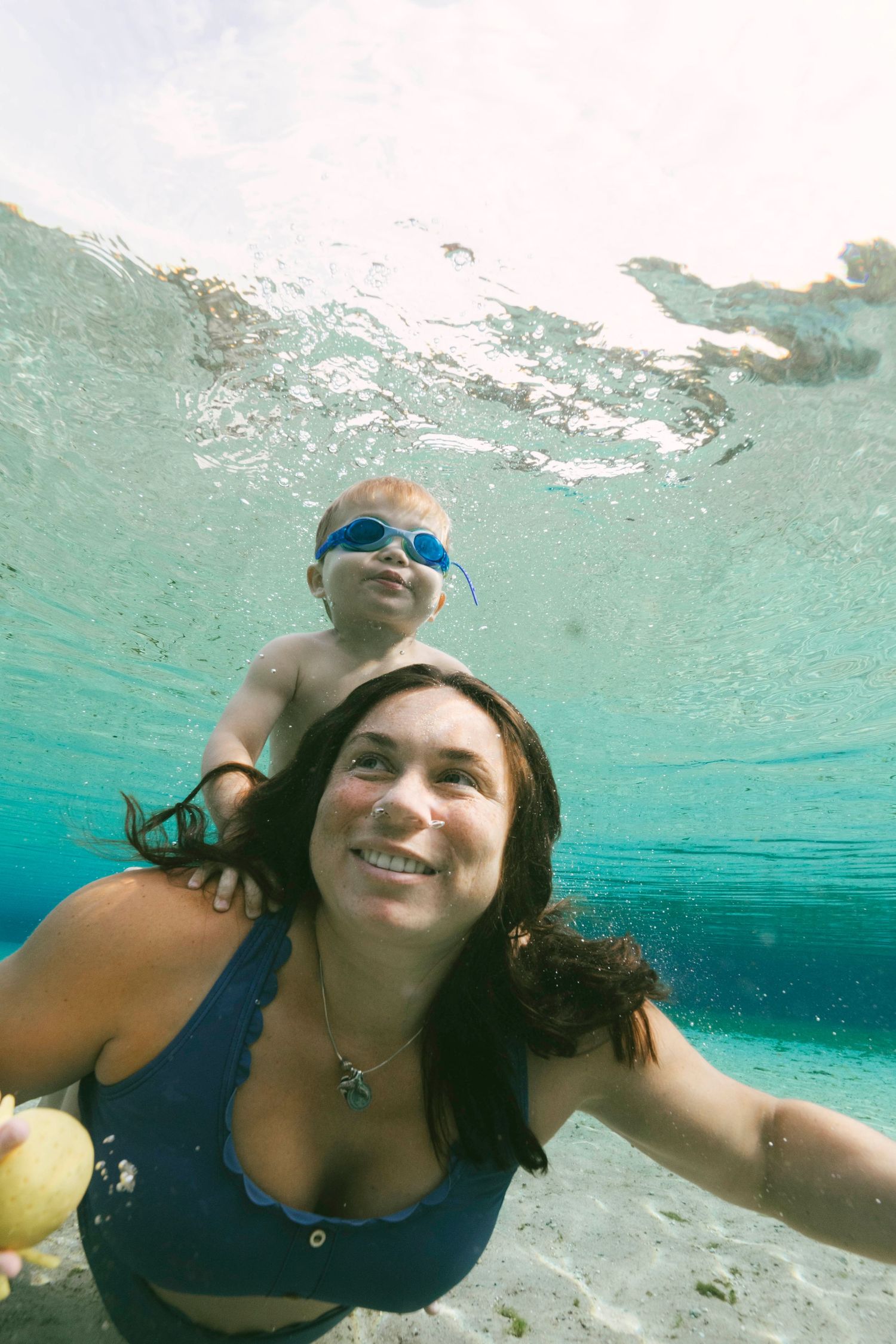 Underwater view of swimmers with blue goggles in crystal clear turquoise water on a bright sunny day.