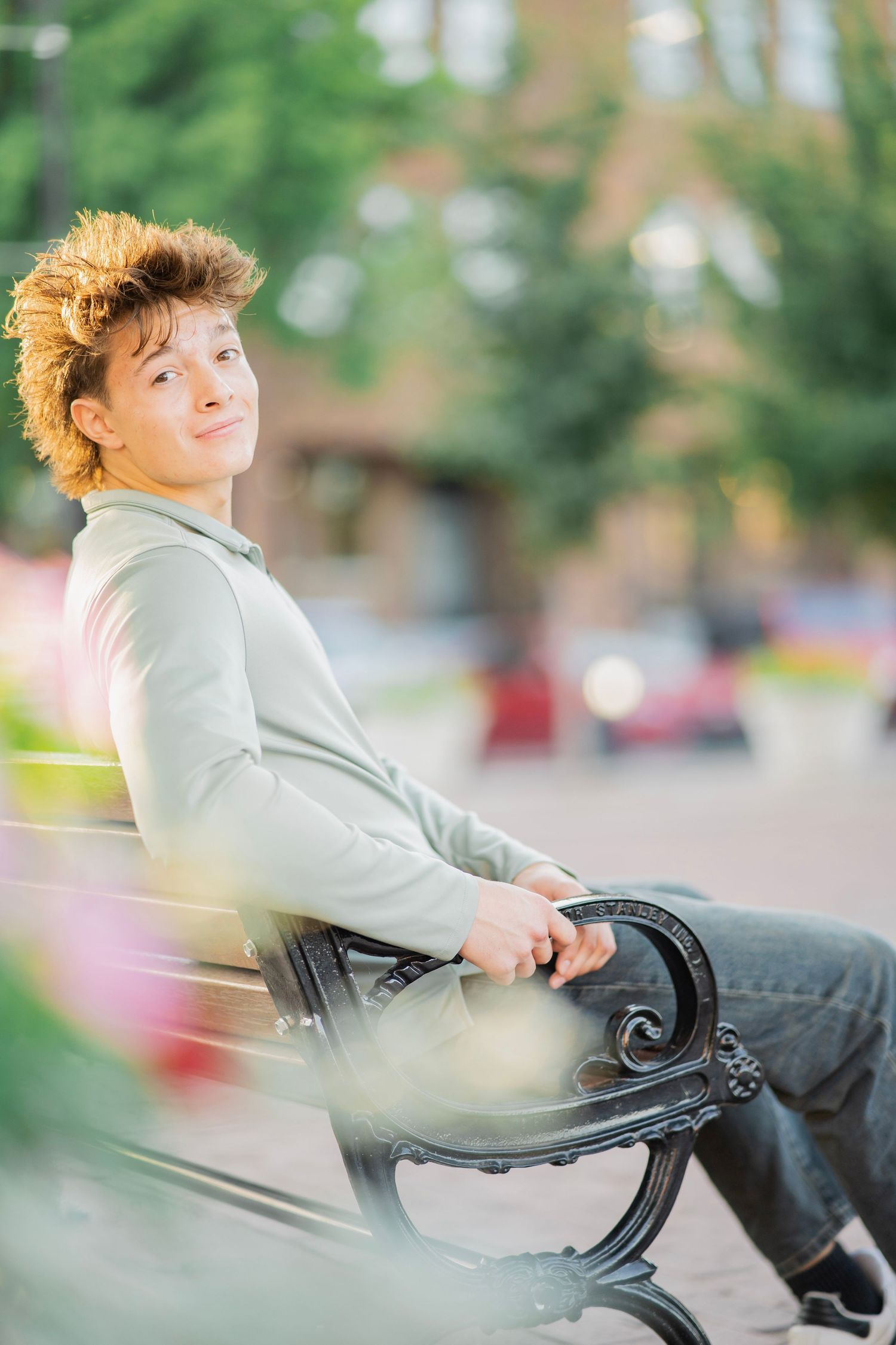 Young man with curly hair sitting relaxed on park bench smiling outdoors.